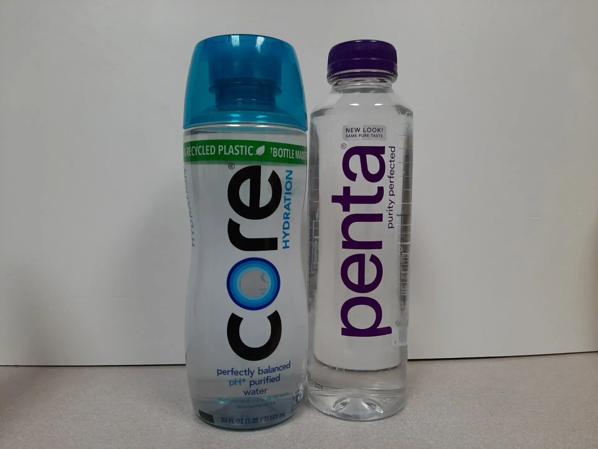 A Core Hydration water bottle with a blue cap sits next to a Penta purified water bottle with a purple cap.