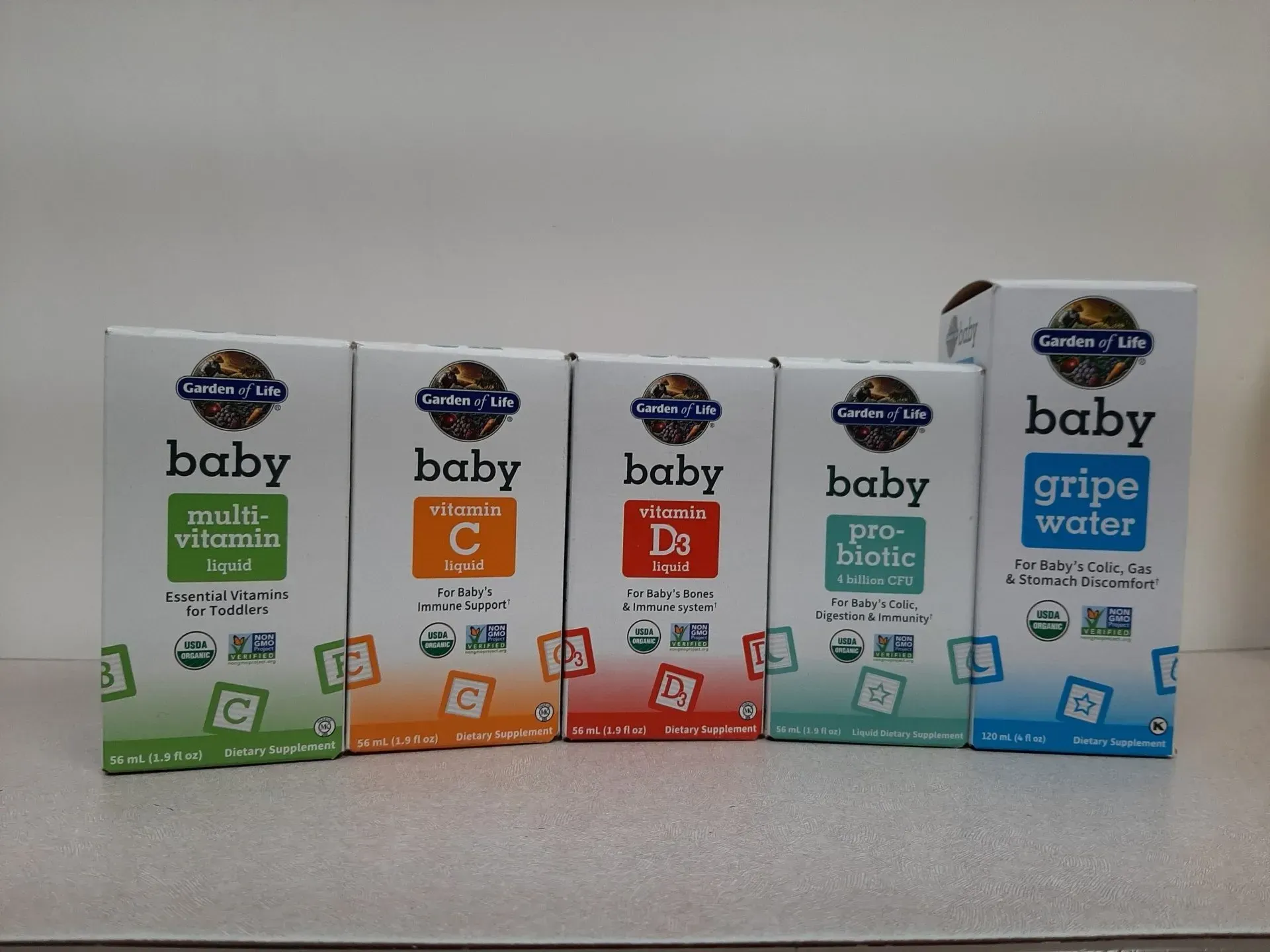 Five Garden of Life baby supplement bottles lined up in a row on a surface against a white wall.