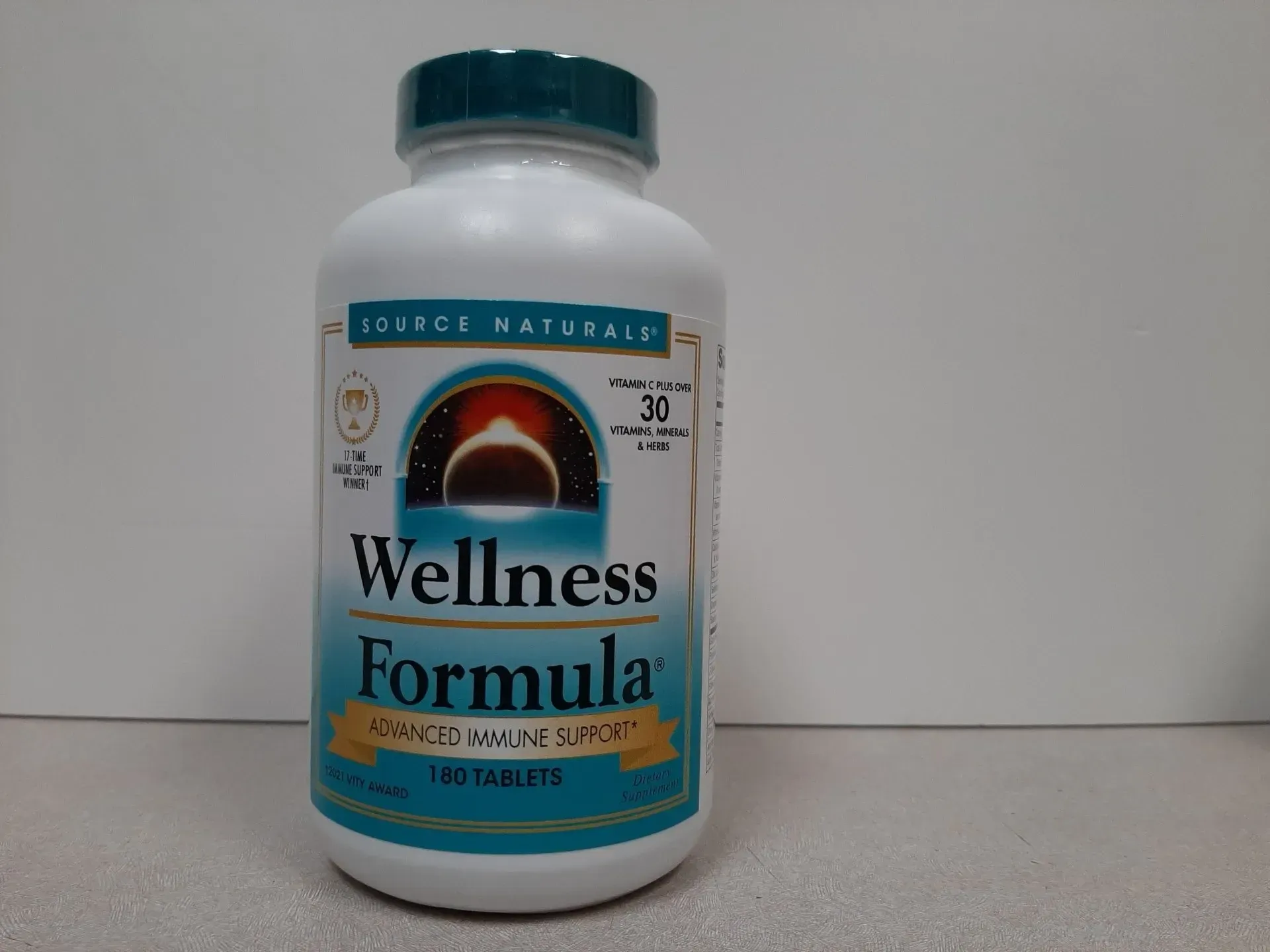 A white plastic bottle of Source Naturals Wellness Formula tablets with a green cap and blue and gold label.