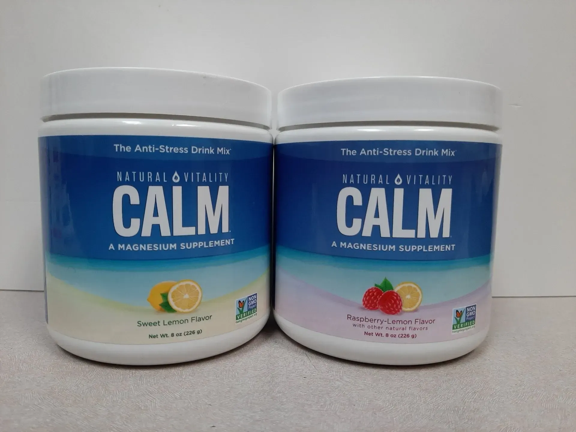 Two white tubs of Natural Vitality CALM magnesium drink mix in Sweet Lemon and Raspberry Lemon flavors.
