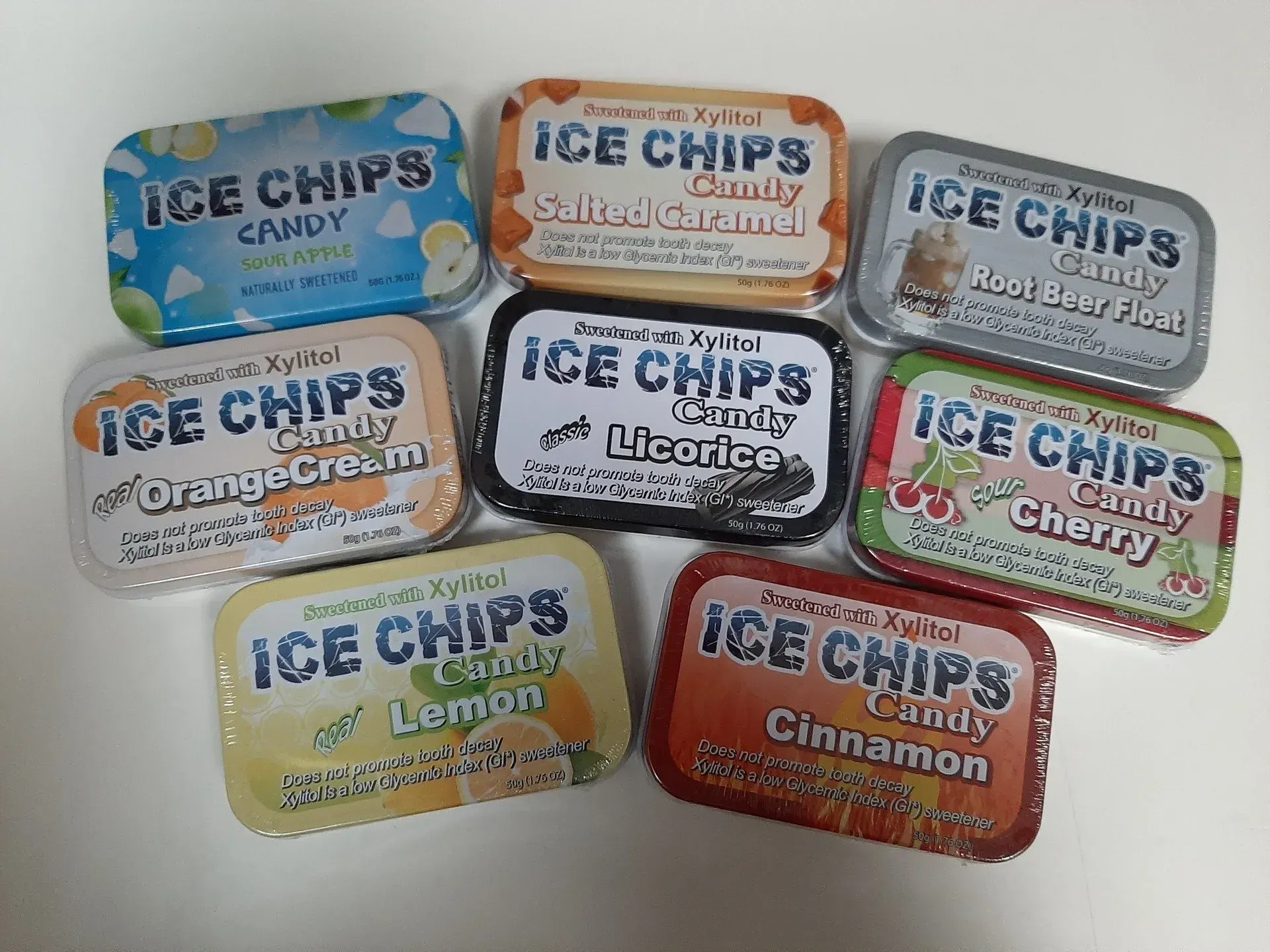 Eight tins of Ice Chips candy in various flavors and colors arranged on a white surface.