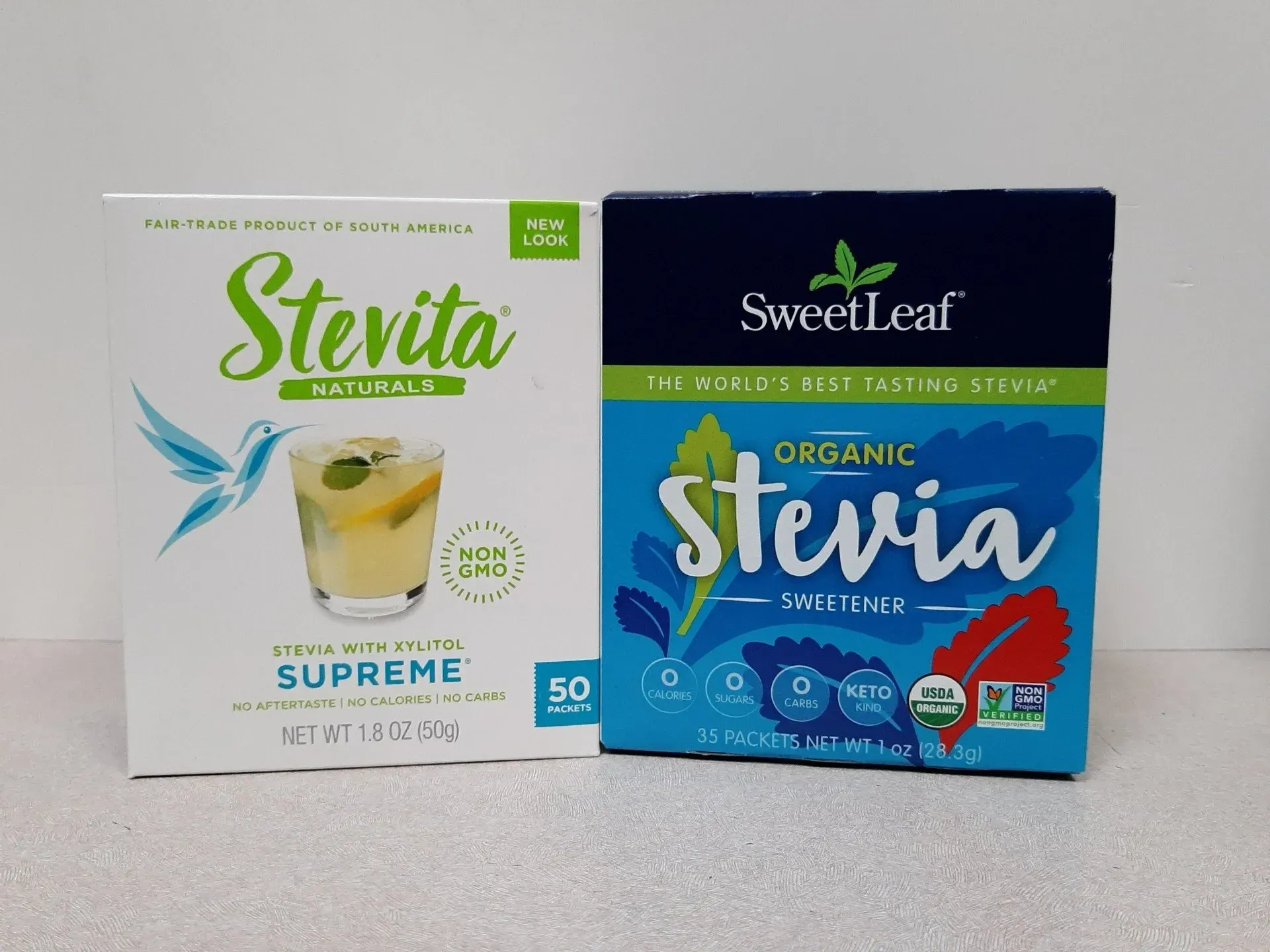 Two boxes of stevia sweetener side-by-side: a white Stevita box on the left and a blue SweetLeaf box on the right.