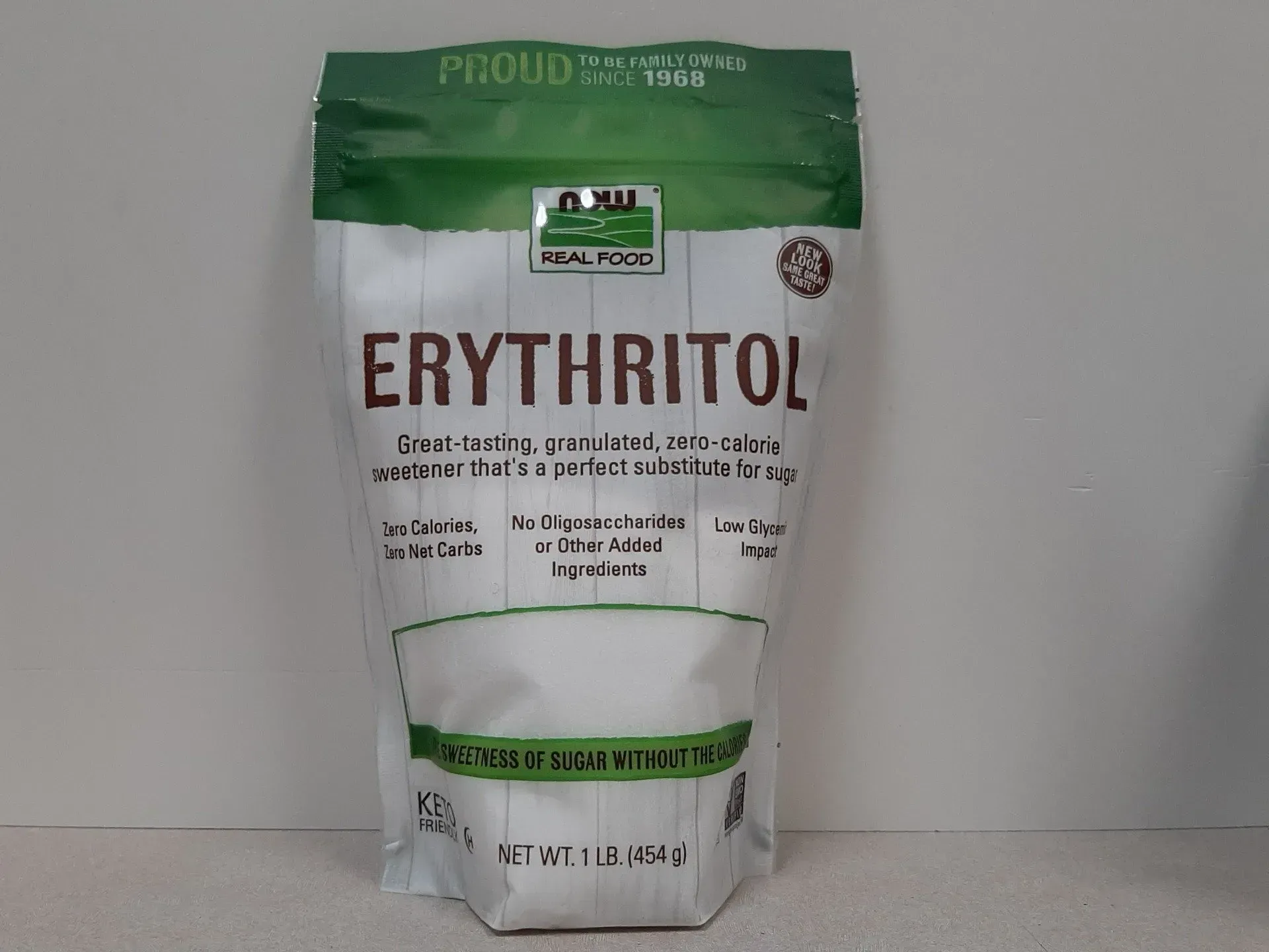 A white, green-topped bag of NOW Real Food Erythritol sweetener standing on a neutral surface.