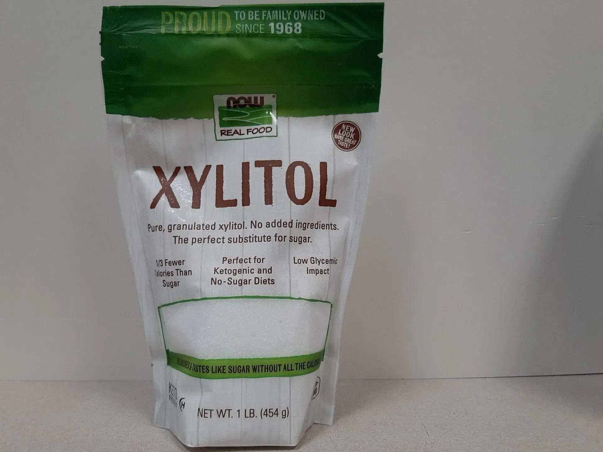 A 1 lb white bag of NOW Real Food Xylitol sweetener with green accents, standing against a plain background.
