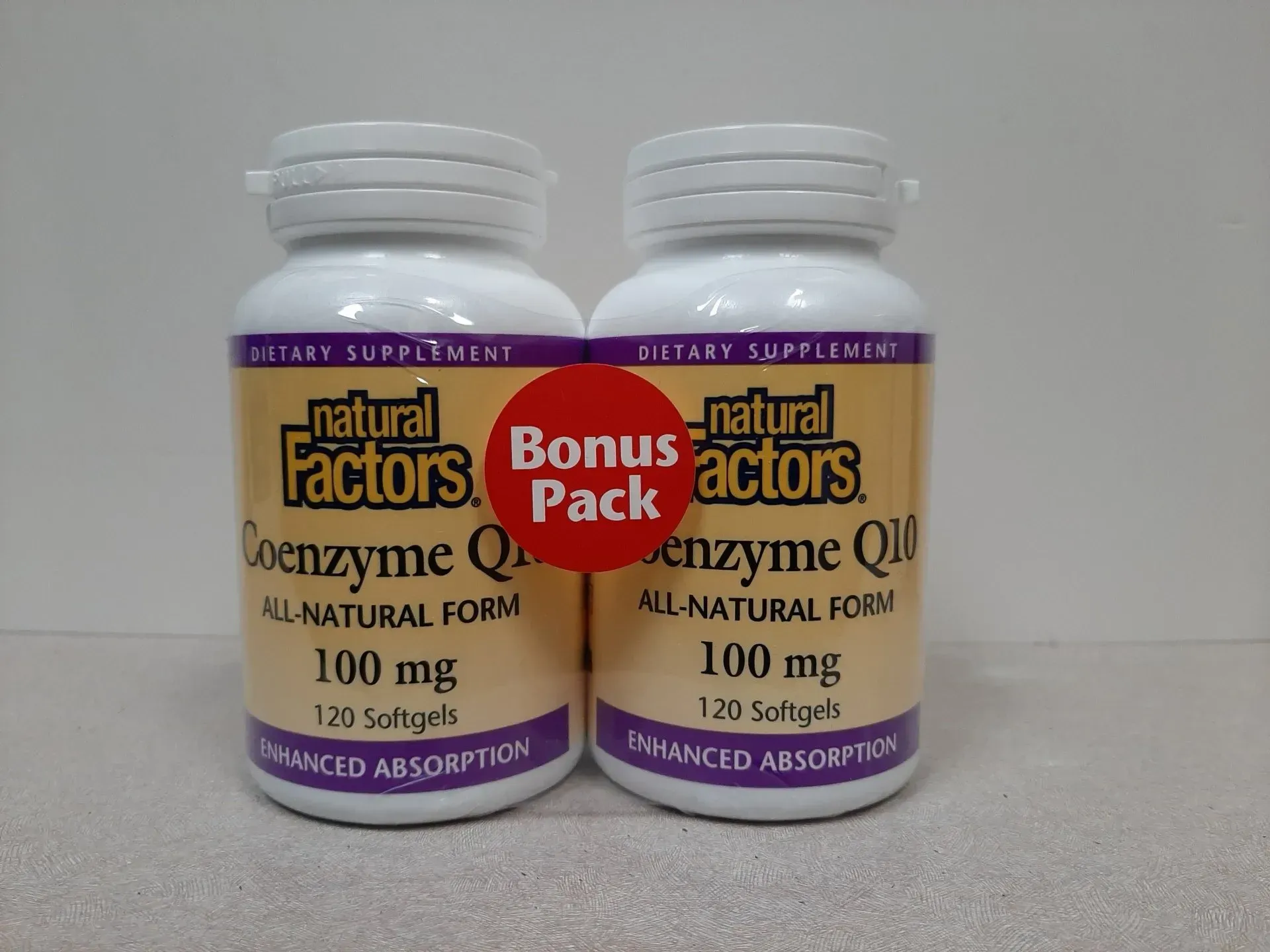 Two white bottles of Natural Factors Coenzyme Q10 100mg softgels with a red