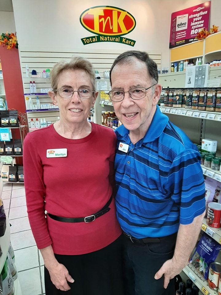 Two people stand smiling inside a store, wearing name tags in front of a 