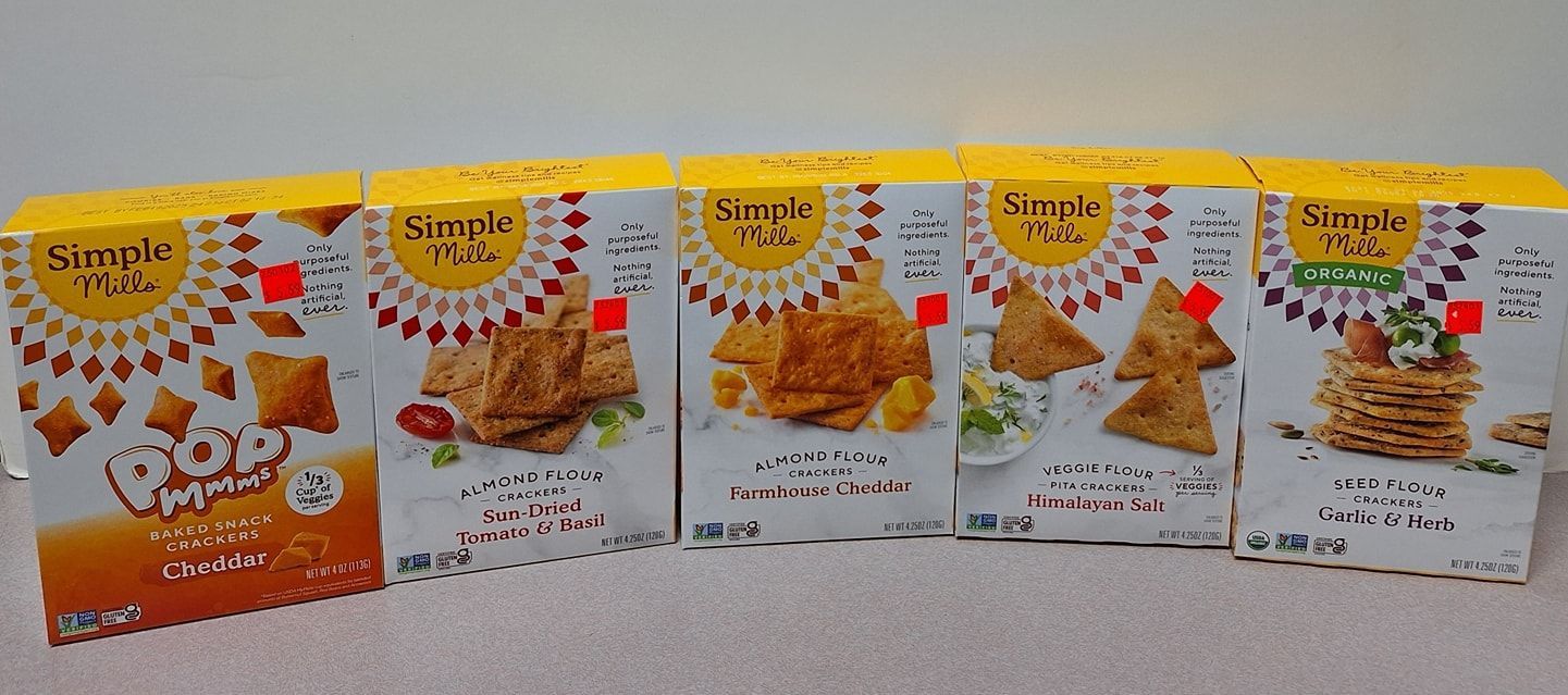 Five boxes of Simple Mills crackers lined up on a surface, showcasing various flavors including almond and flax options.