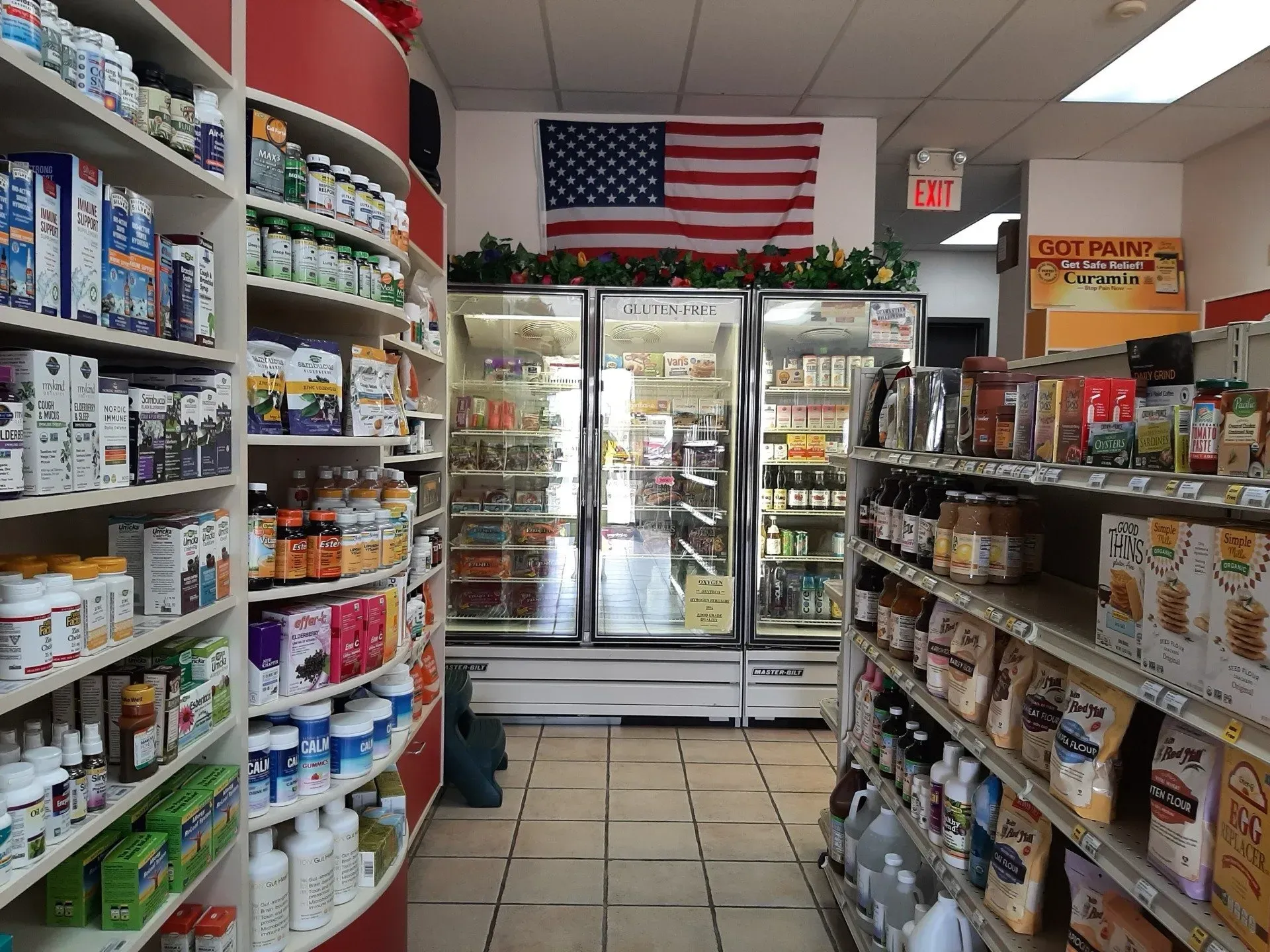 Grocery store interior with shelves of products, refrigerators, and American flag.