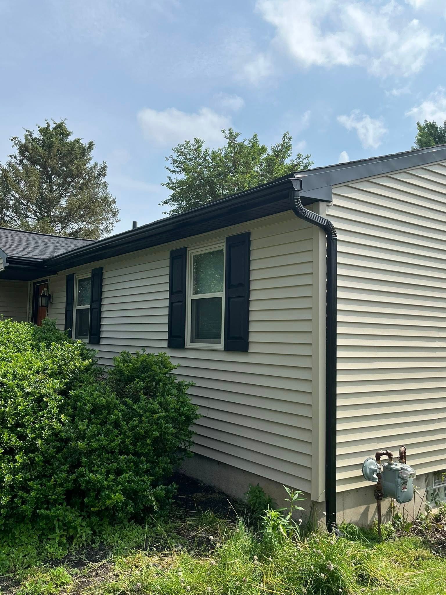 Black gutters installed on a pale yellow house in Rochester area