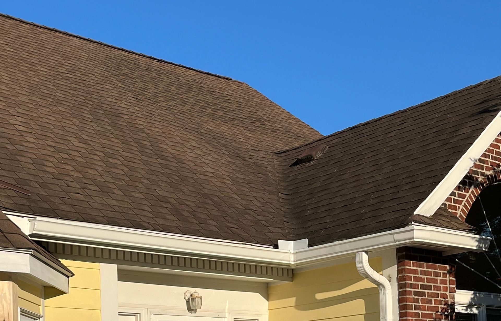 A new gutter system installed on a house with yellow siding and a black roof