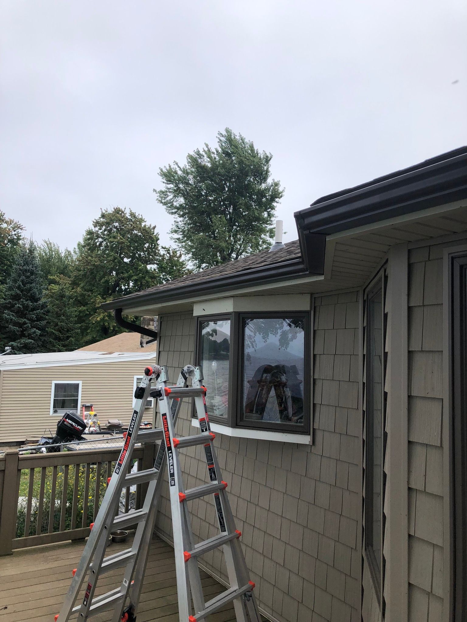 A ladder is set up next to a gray house in the middle of a gutter repair service