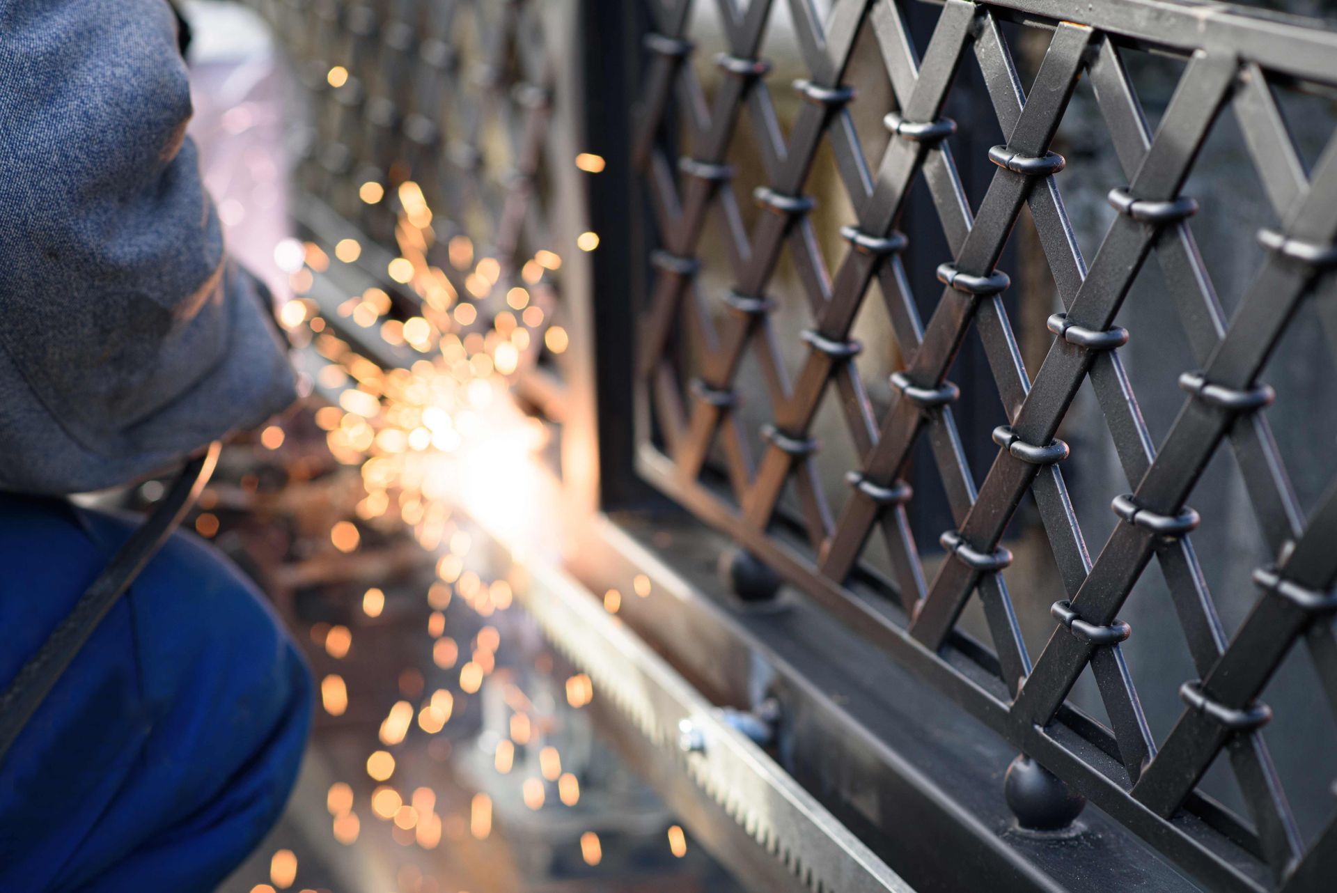Person welding a metal fence, with bright sparks flying in a workshop