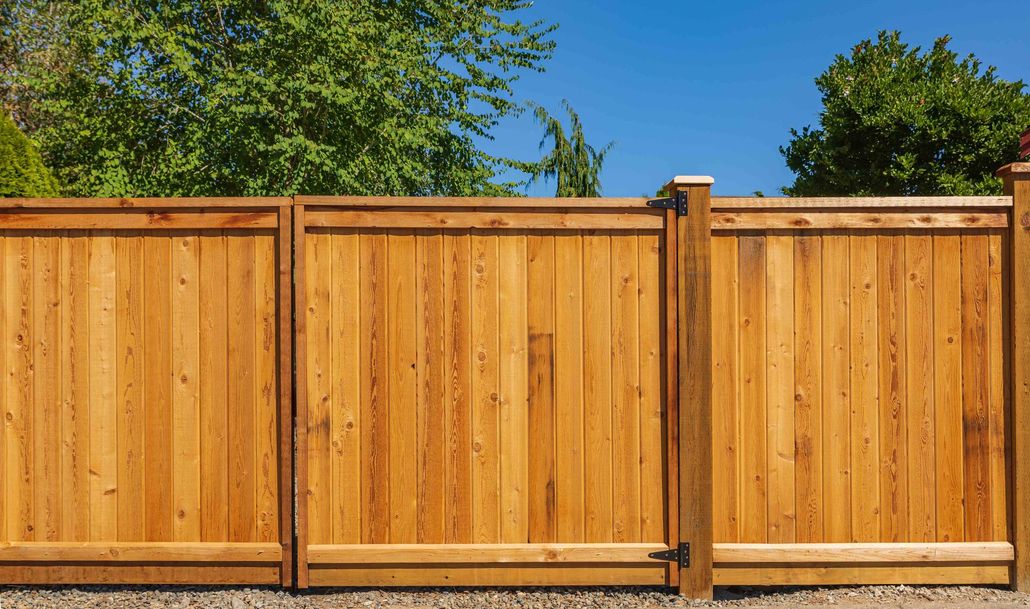 Wooden privacy fence with tan panels and brown posts under a clear blue sky