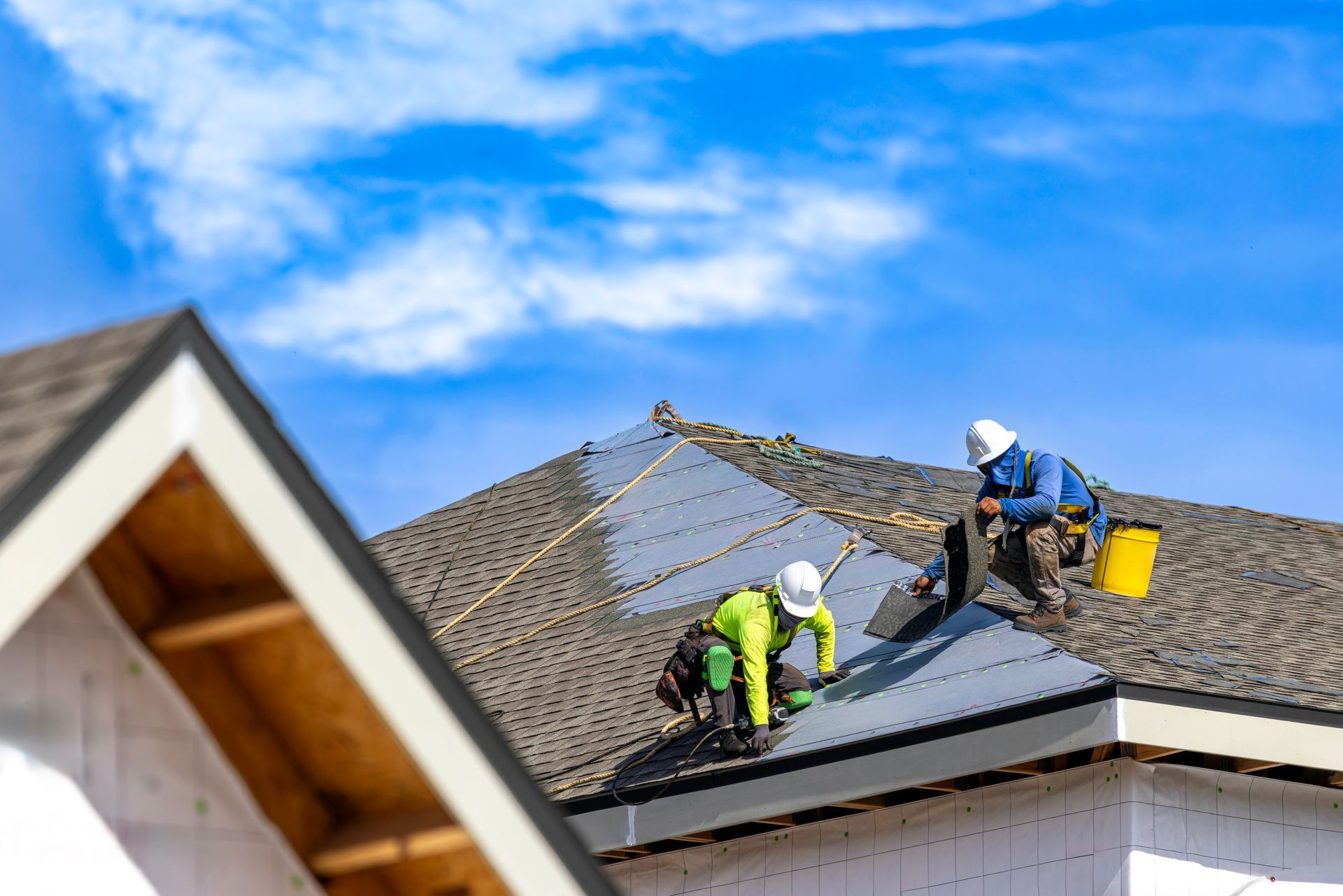Two roofers in hard hats installing shingles on a residential roof.