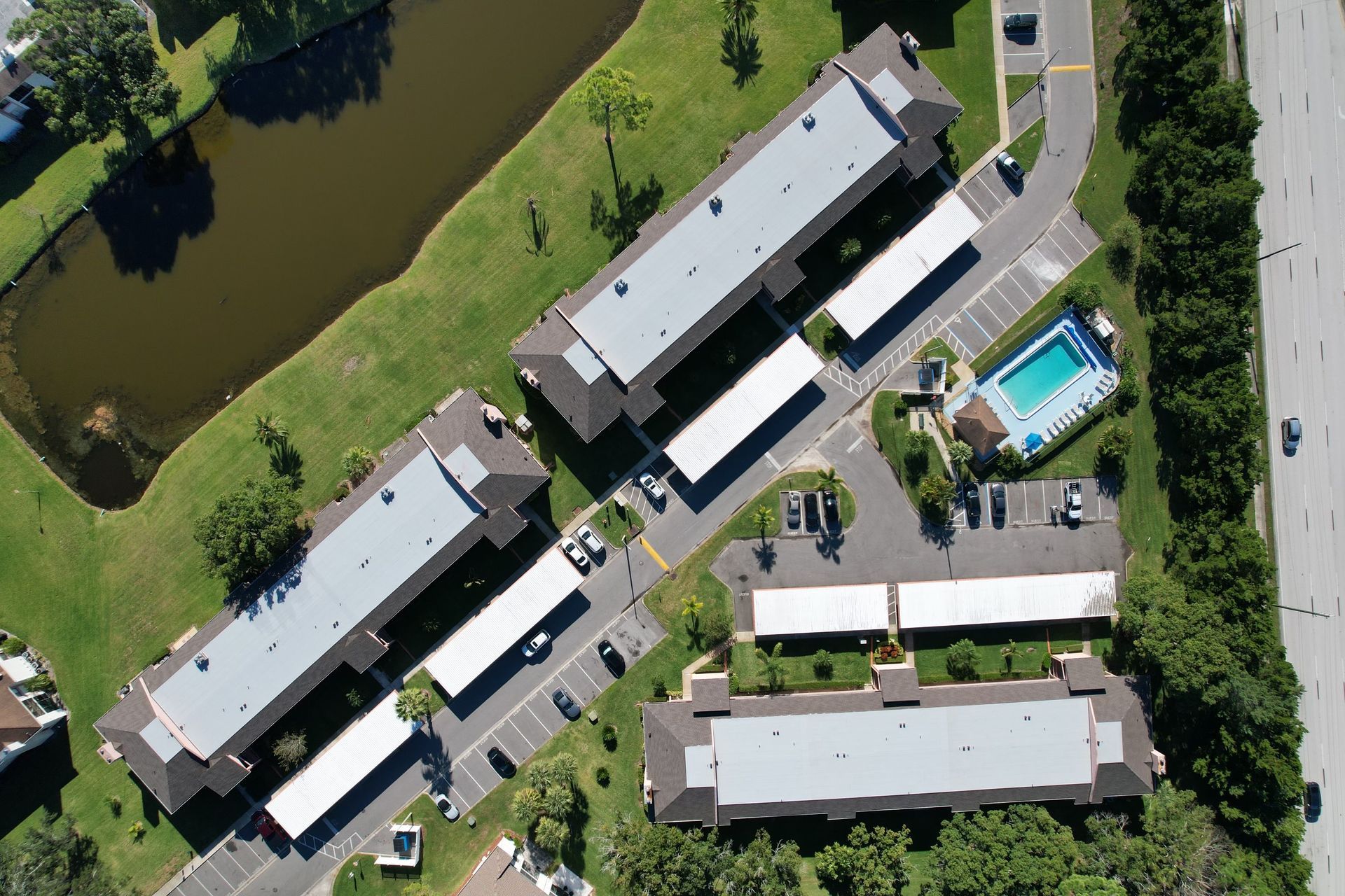 Aerial view of apartment complex with pond, swimming pool, parking, and a road. Aerial view of apartment complex with pond, swimming pool, parking, and a road.