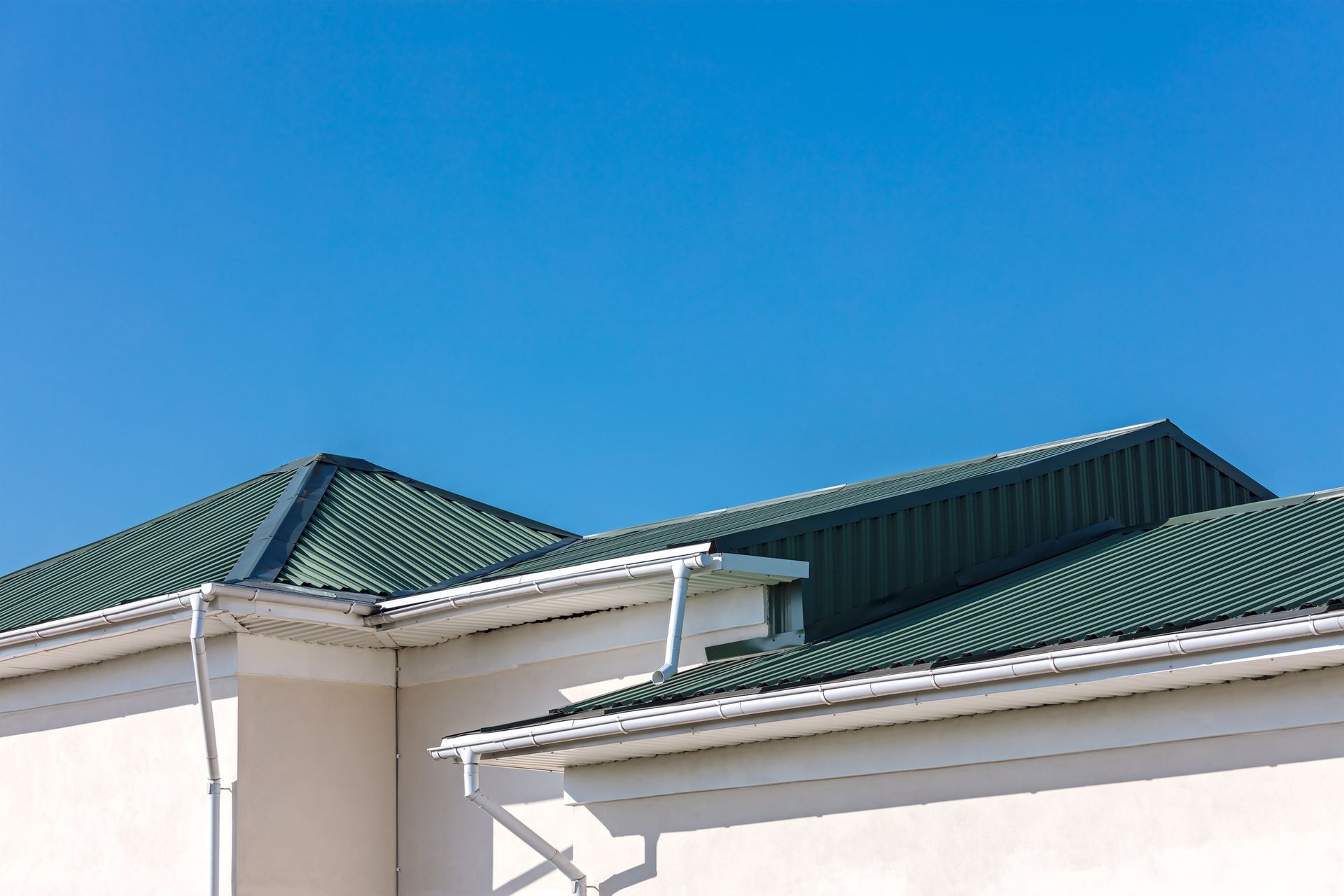 Green corrugated metal roof with white gutters against a clear blue sky.