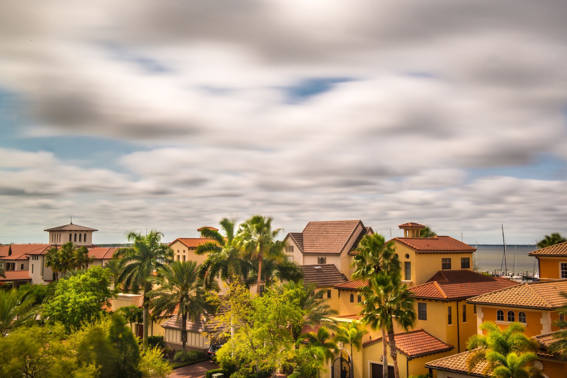 A coastal community with terracotta roofs and palm trees under a cloudy sky. A coastal community with terracotta roofs and palm trees under a cloudy sky.