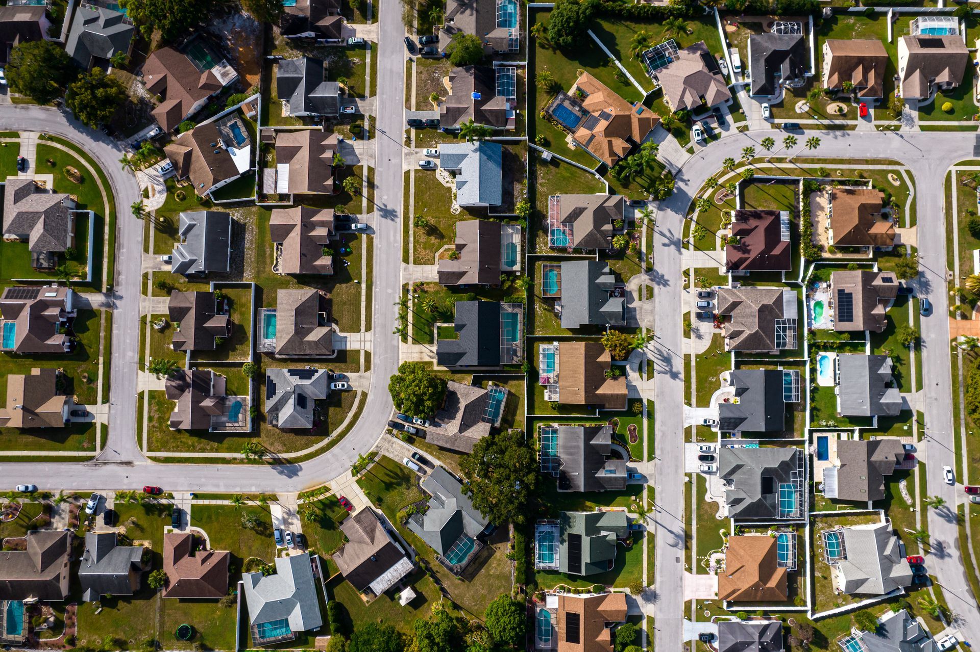 Aerial view of a suburban neighborhood with houses, streets, and green lawns; various roof colors. Aerial view of a suburban neighborhood with houses, streets, and green lawns; various roof colors.