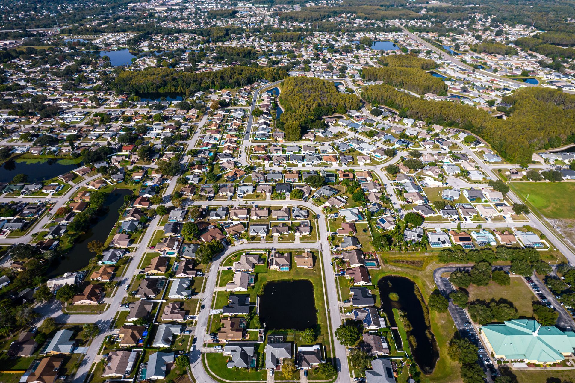 Aerial view of a suburban neighborhood with townhomes lining a lake, surrounded by green trees.