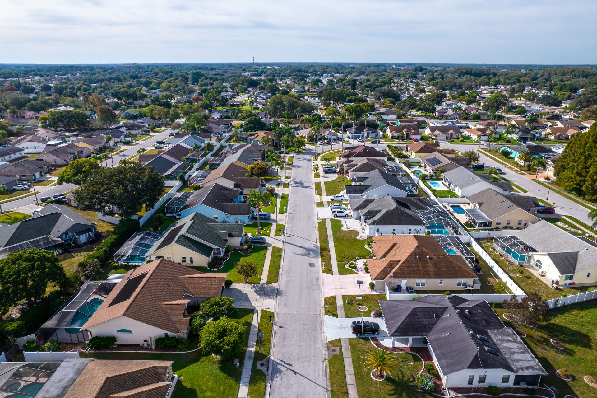 Aerial view of suburban houses with green lawns and trees lining the streets under a blue sky. Aerial view of suburban houses with green lawns and trees lining the streets under a blue sky.