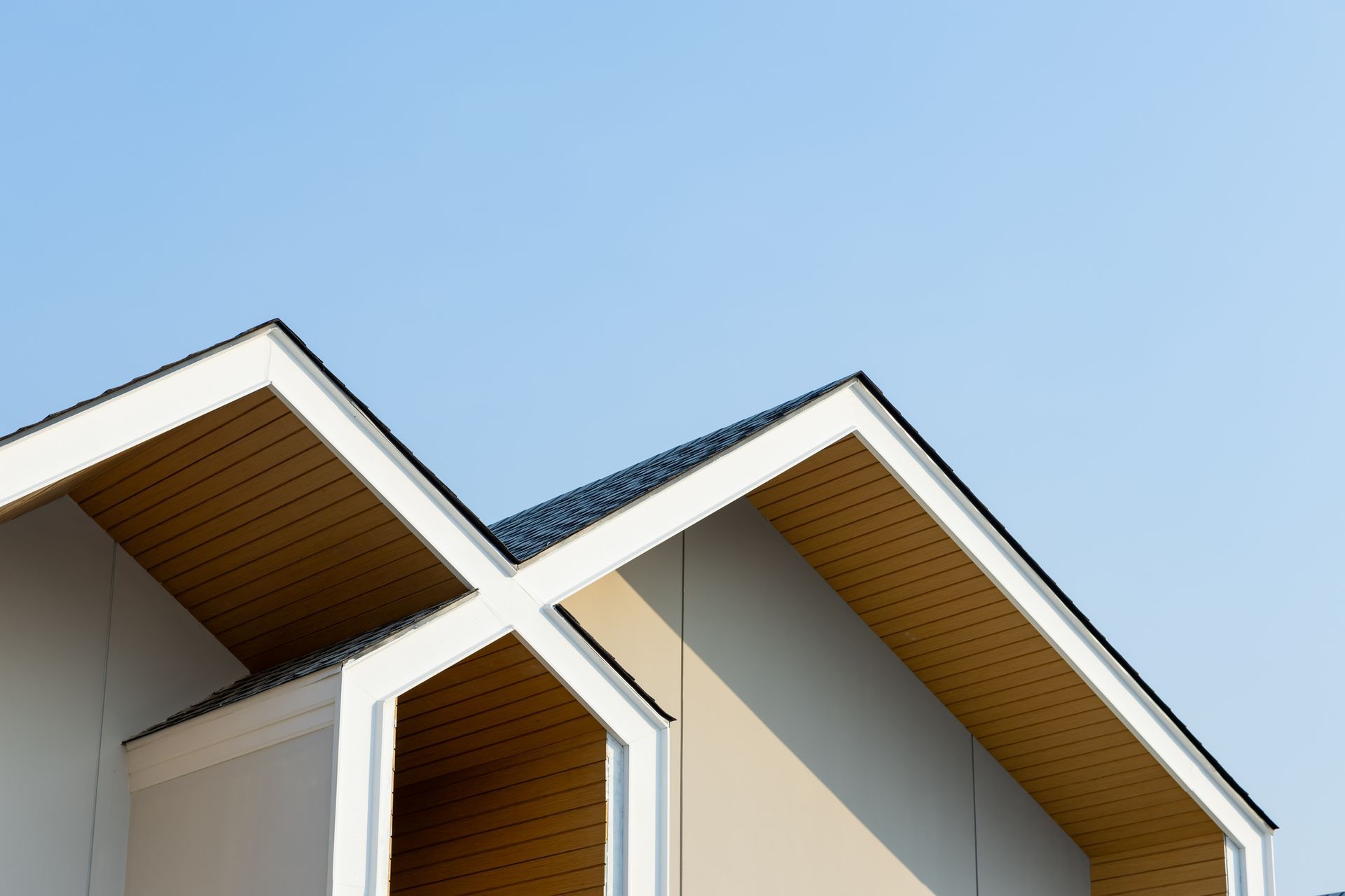 White and beige house roof against a clear blue sky.
