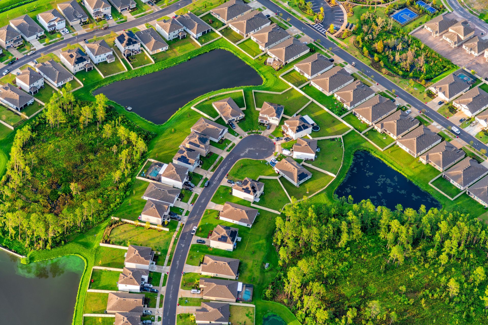 Aerial view of a suburban neighborhood with houses, roads, ponds, and greenery. Aerial view of a suburban neighborhood with houses, roads, ponds, and greenery.