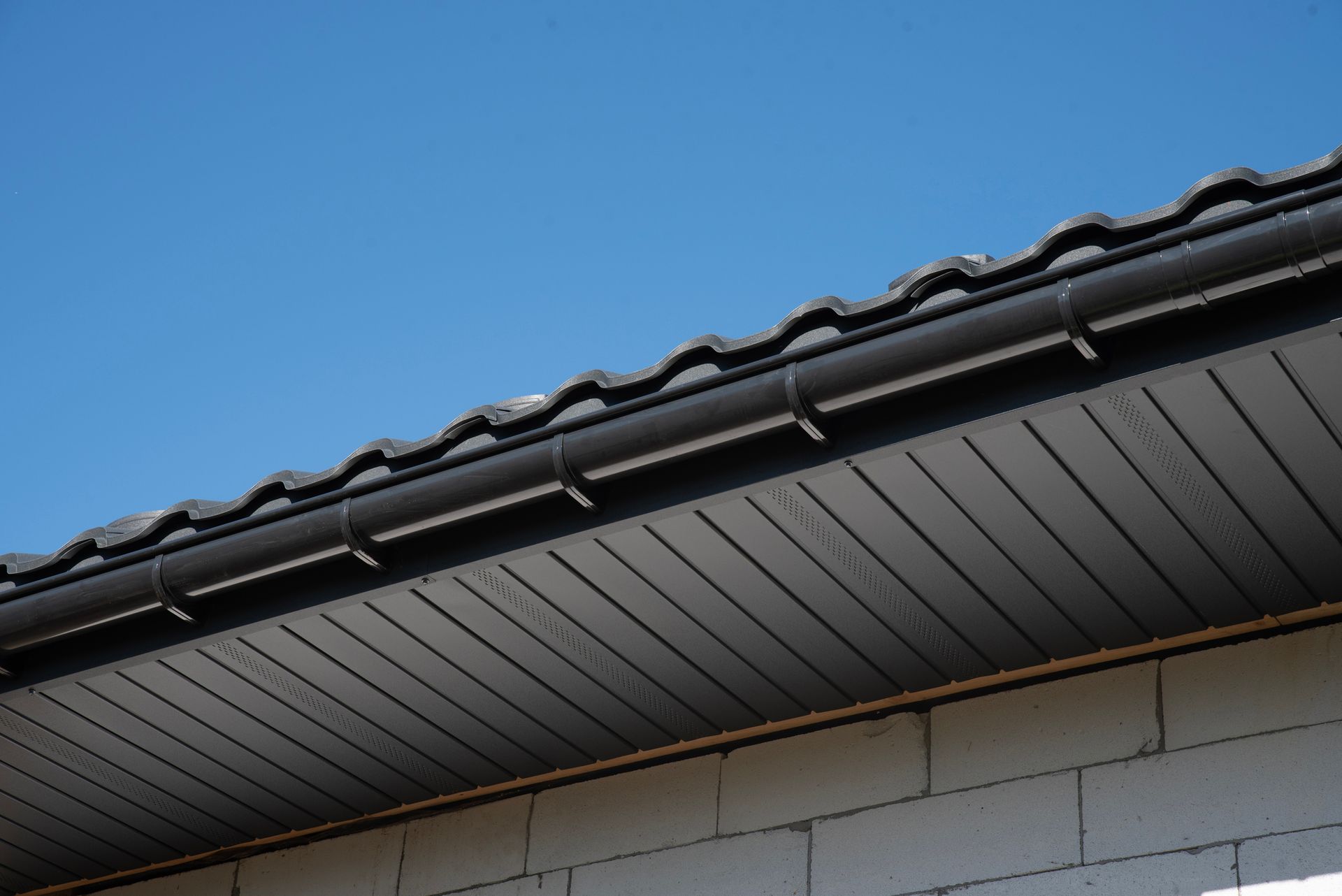 Black roof with gutter, soffit, and light blue sky.