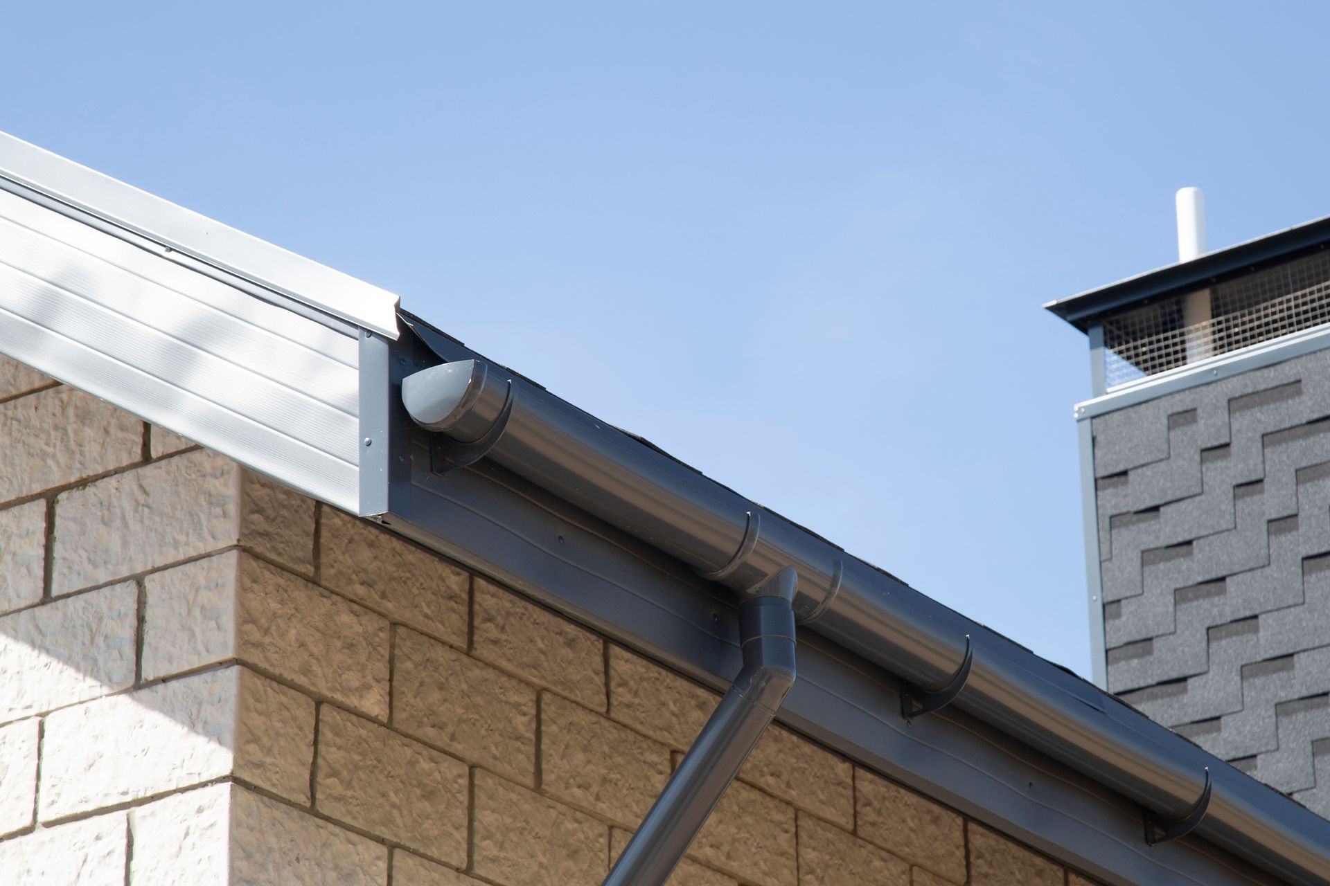 Gray rain gutter along the edge of a brick building under a blue sky.