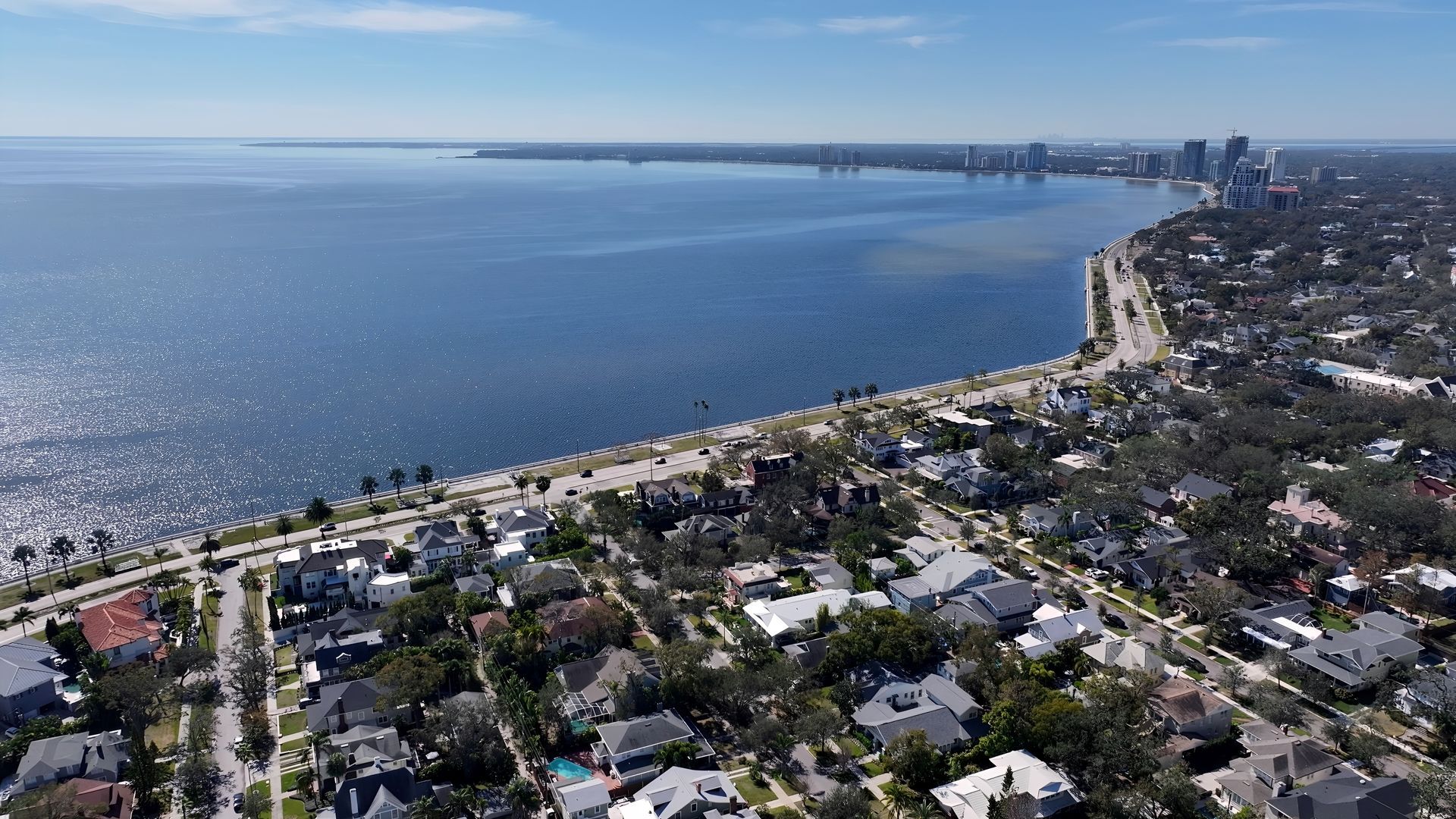 Aerial view of a coastal city with a body of water, road, and buildings under a blue sky. Aerial view of a coastal city with a body of water, road, and buildings under a blue sky.