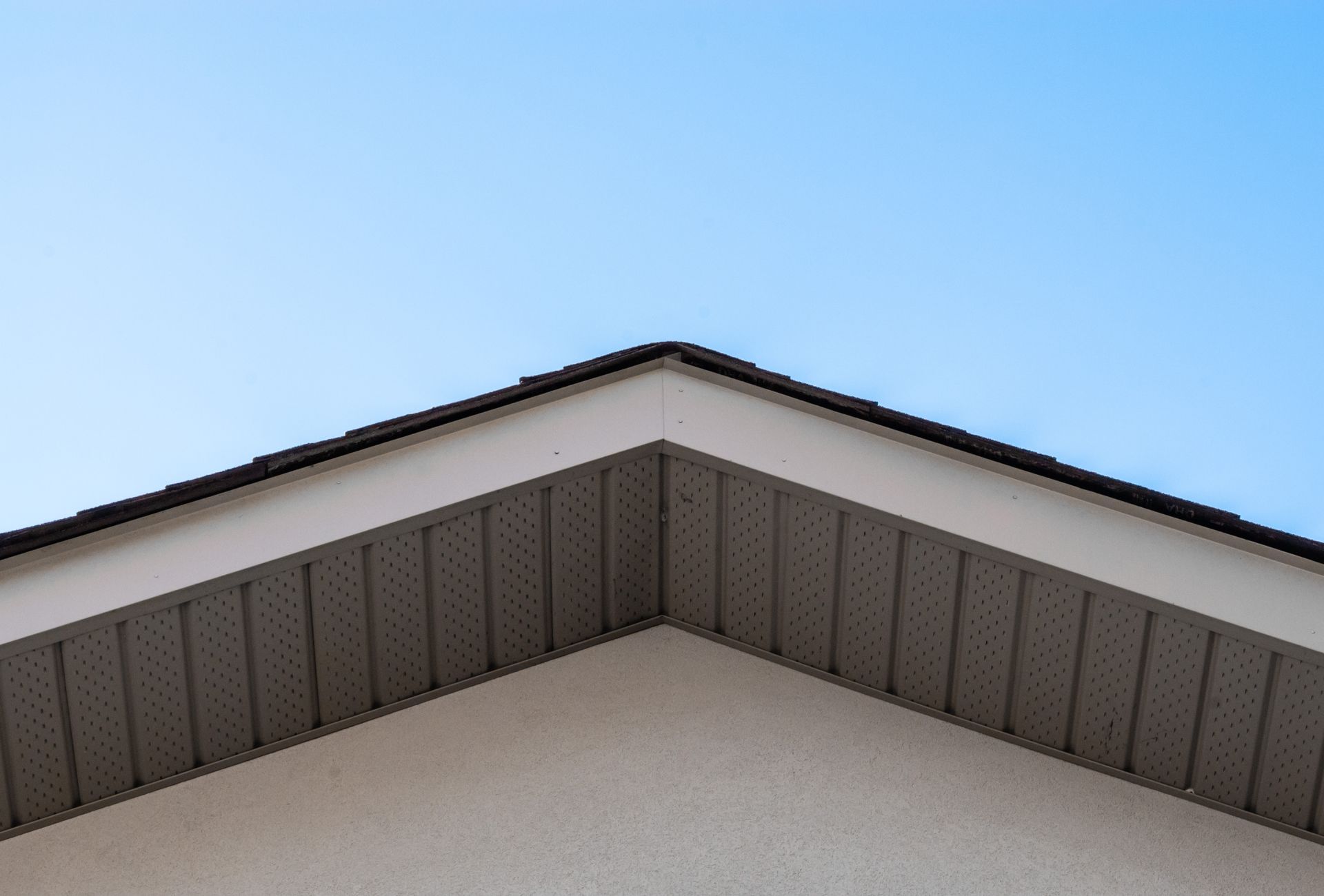 Close-up of a house roof, white exterior, gray under-roof, with a blue sky background. Close-up of a house roof, white exterior, gray under-roof, with a blue sky background.