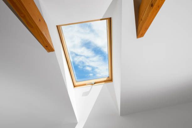 Skylight in a white ceiling with wooden beams, revealing a blue sky with clouds.