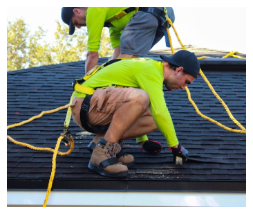 Two roofers in neon green shirts and safety harnesses working on a dark asphalt shingle roof.