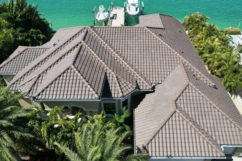 Brown tile-roofed house overlooking the ocean and dock with boats, surrounded by palm trees. Brown tile-roofed house overlooking the ocean and dock with boats, surrounded by palm trees.