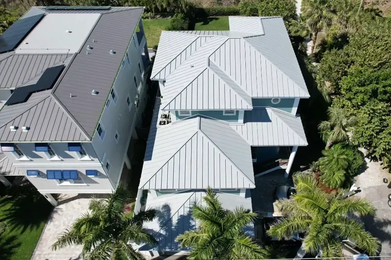 Aerial view of two light blue houses with silver metal roofs, surrounded by trees. Aerial view of two light blue houses with silver metal roofs, surrounded by trees.