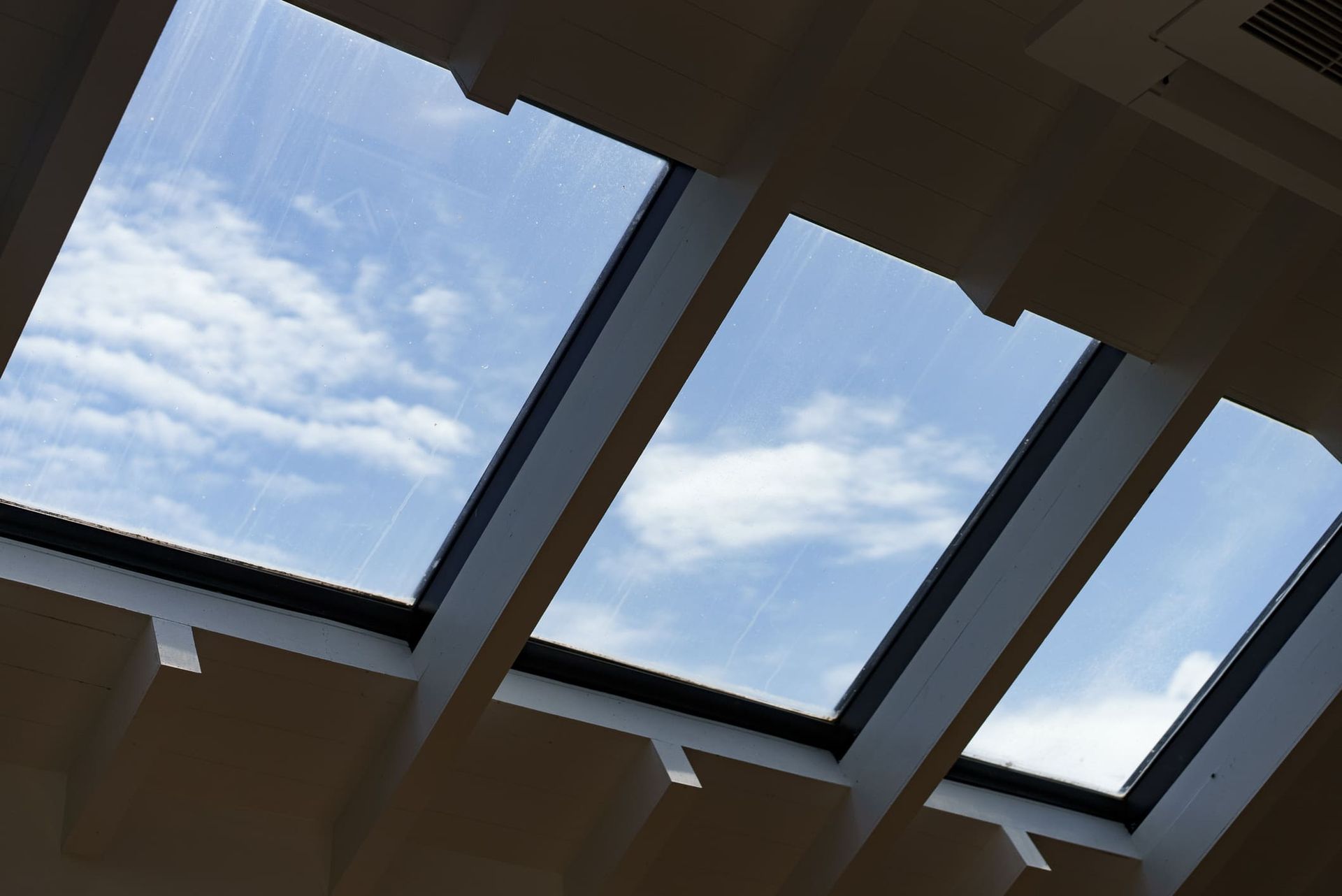 Skylights in a ceiling, angled view of a blue sky with clouds.