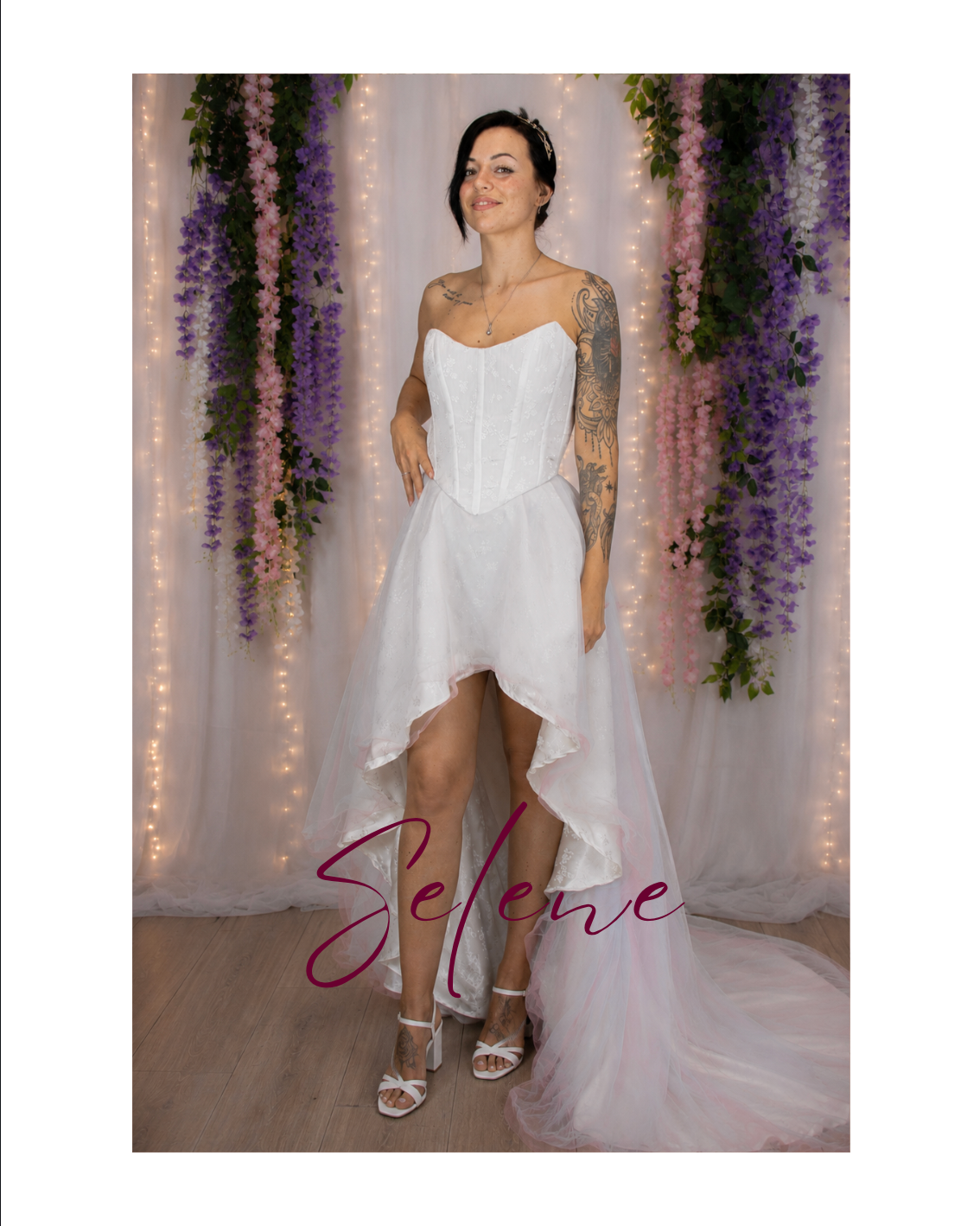 Woman in a white dress and veil posing against a floral backdrop with lights