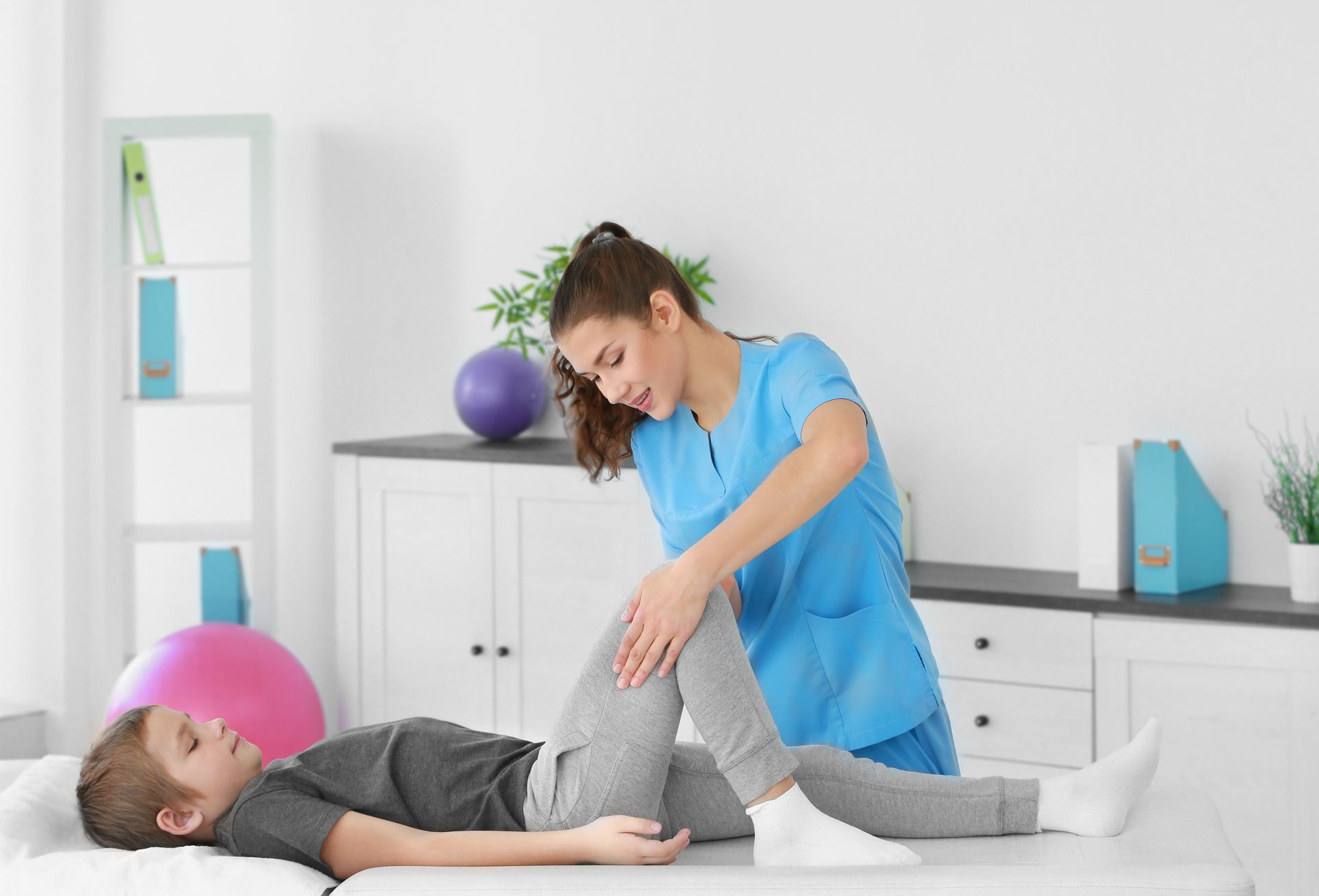 A woman is stretching a child 's leg on a table.