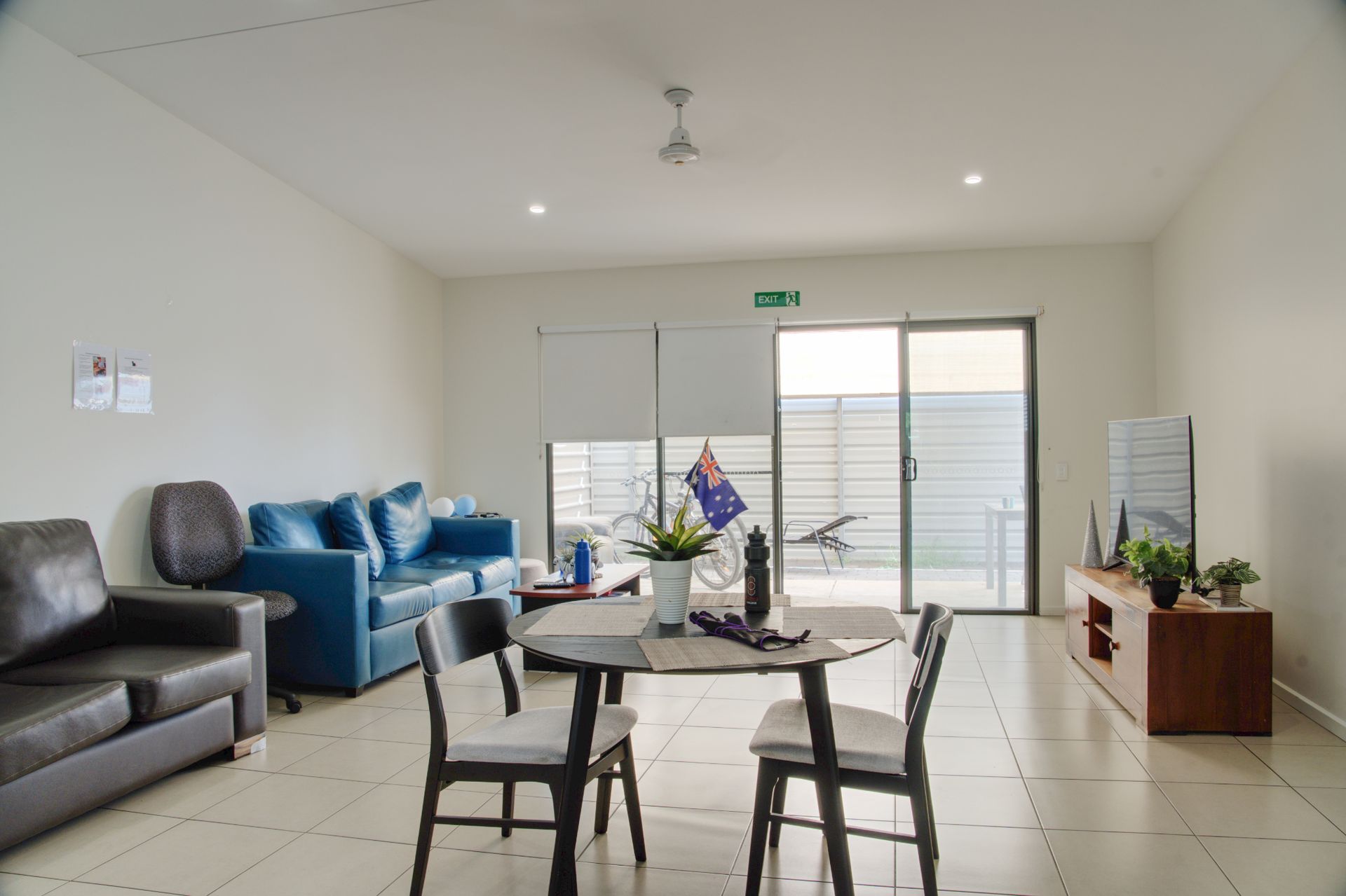 A brightly lit living and dining area with a blue couch, a dark brown sofa, a round dining table, and a TV console.