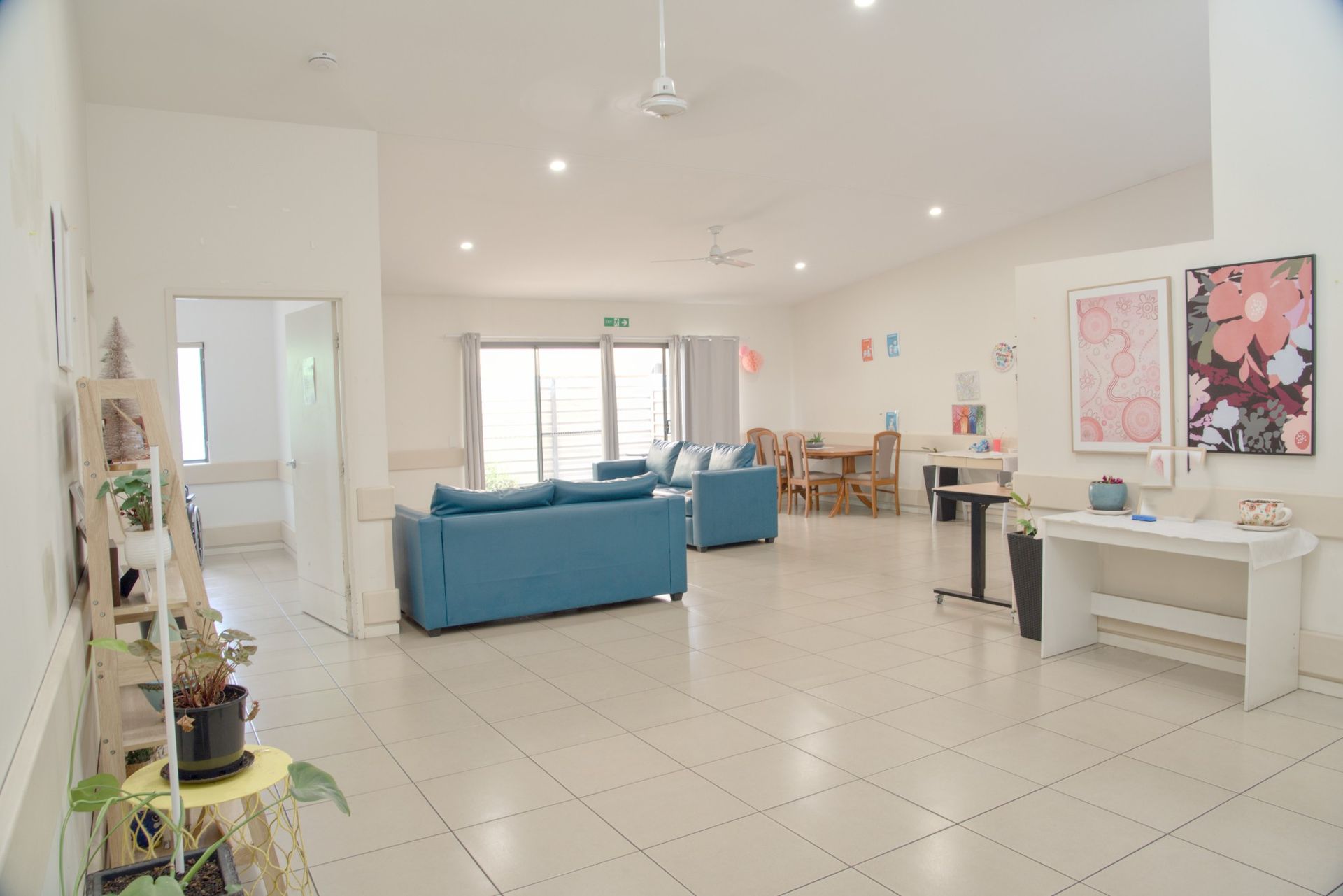 A modern lounge with two blue sofas, a wall-mounted television, a wooden coffee table, and large glass doors.
