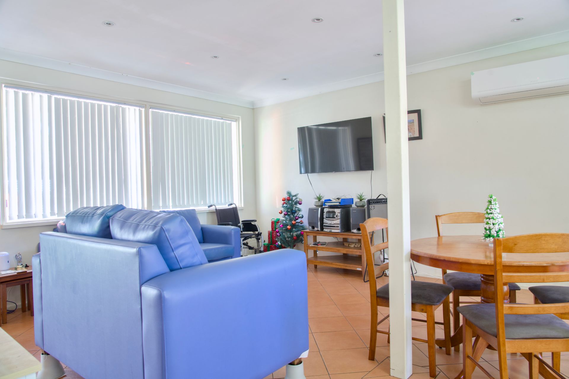 A bedroom with a wooden single bed, a small plant on a side table, and a turtle-patterned orange curtain on the window.