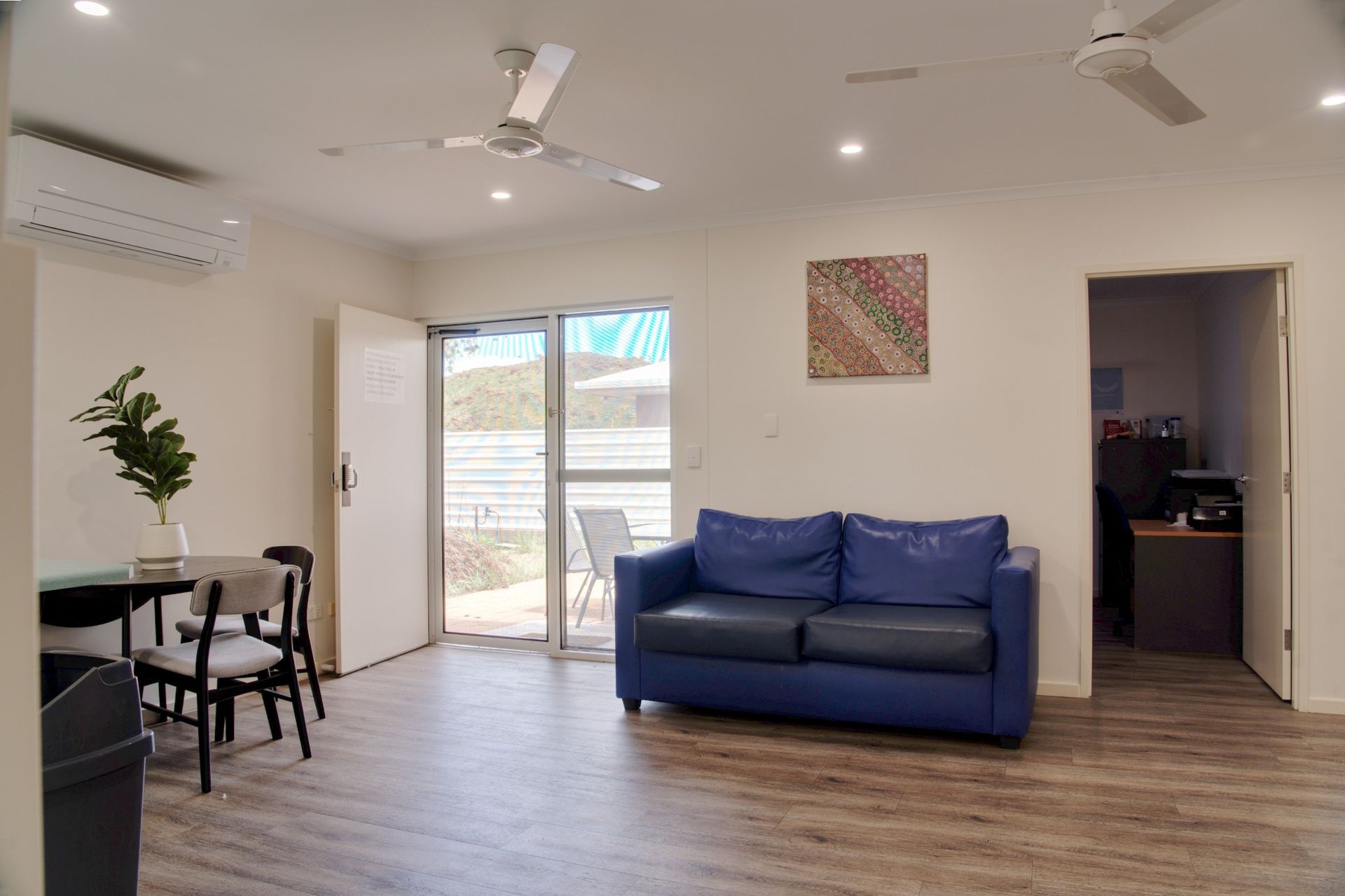Single-story beige row houses with grey gabled roofs and pillars under a blue sky with white clouds.