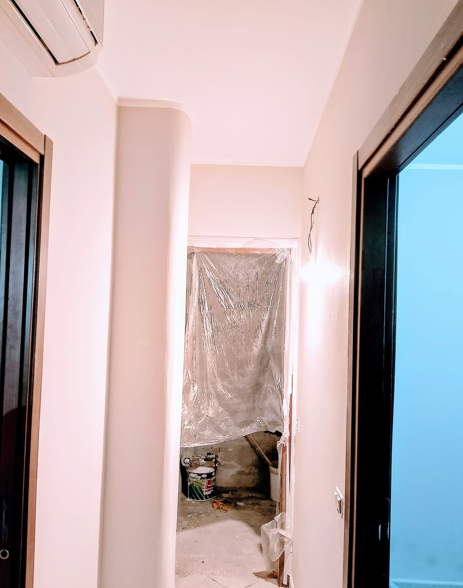 Un corridoio interno con pareti chiare, che conduce a una porta con all'interno un'area di costruzione grezza e non rifinita.