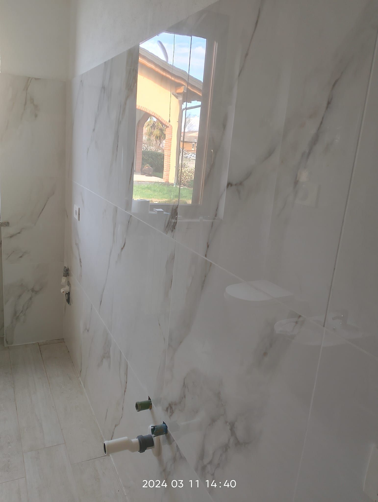 Una parete del bagno moderna, parzialmente piastrellata, con piastrelle effetto marmo bianco e rubinetteria per il lavabo.