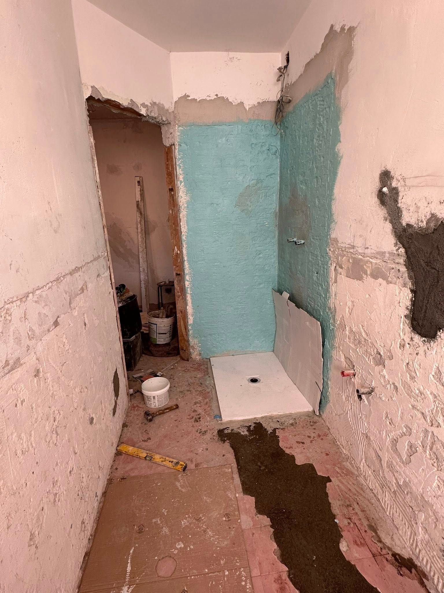 Bagno in fase di ristrutturazione con pareti a vista, box doccia blu impermeabilizzato e piatto doccia bianco sul pavimento.