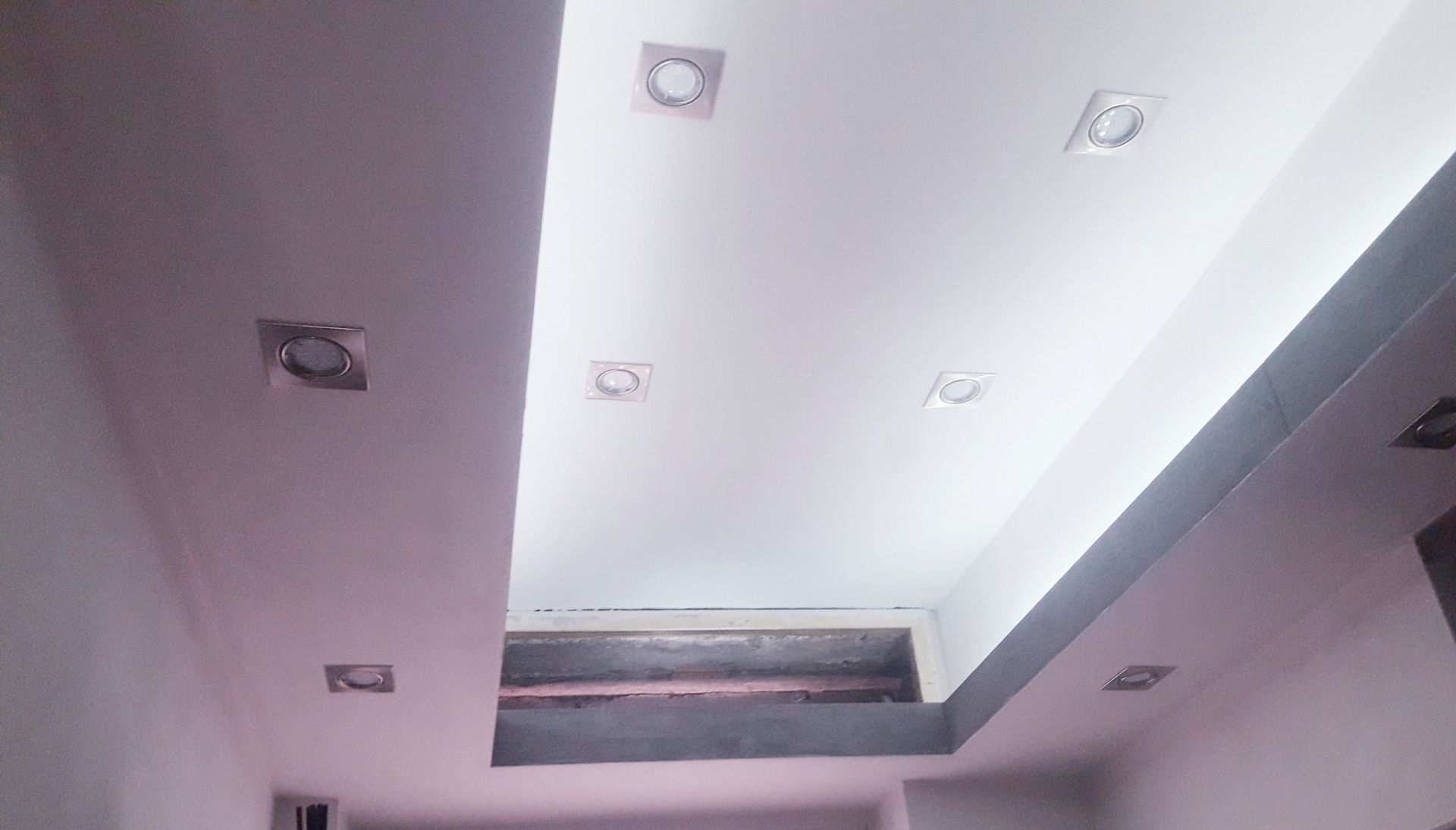 Un controsoffitto bianco con faretti quadrati incassati e un'apertura rettangolare, incorniciata da dettagli dipinti di grigio.
