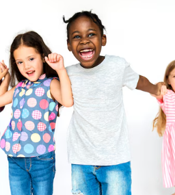 Niños sonriendo y tomados de la mano sobre un fondo blanco; uno con una blusa de lunares, el otro con una camisa blanca.