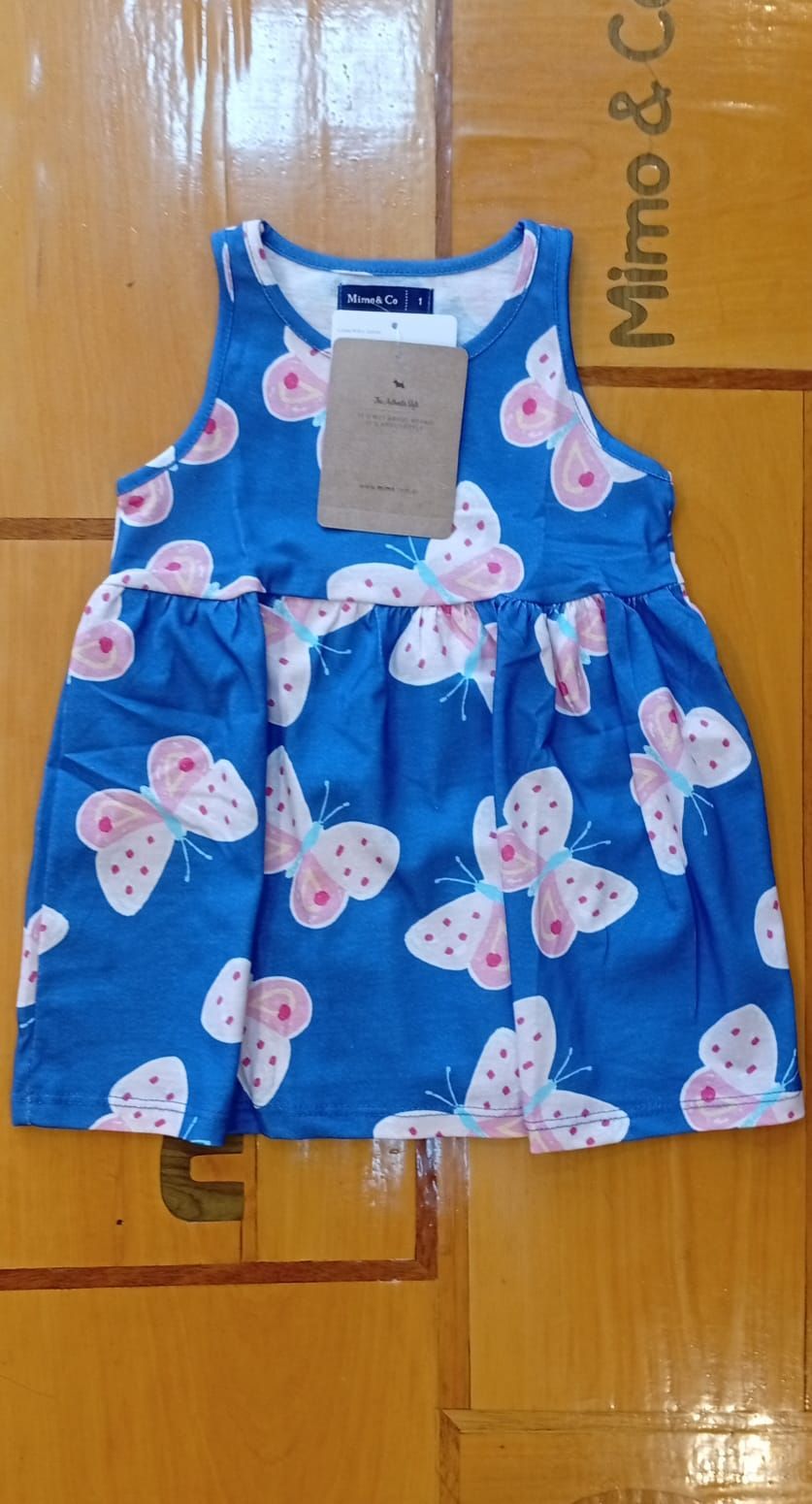 Vestido azul con estampado de mariposas y etiqueta sobre una superficie de madera.