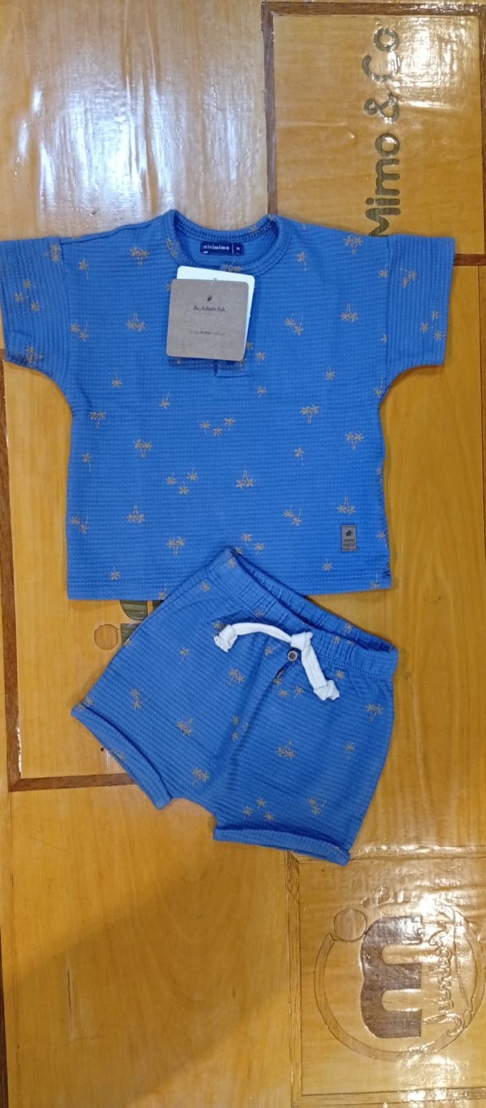 Conjunto azul de bebé, camiseta y pantalones cortos, con etiqueta de precio, colocado sobre una superficie de madera.