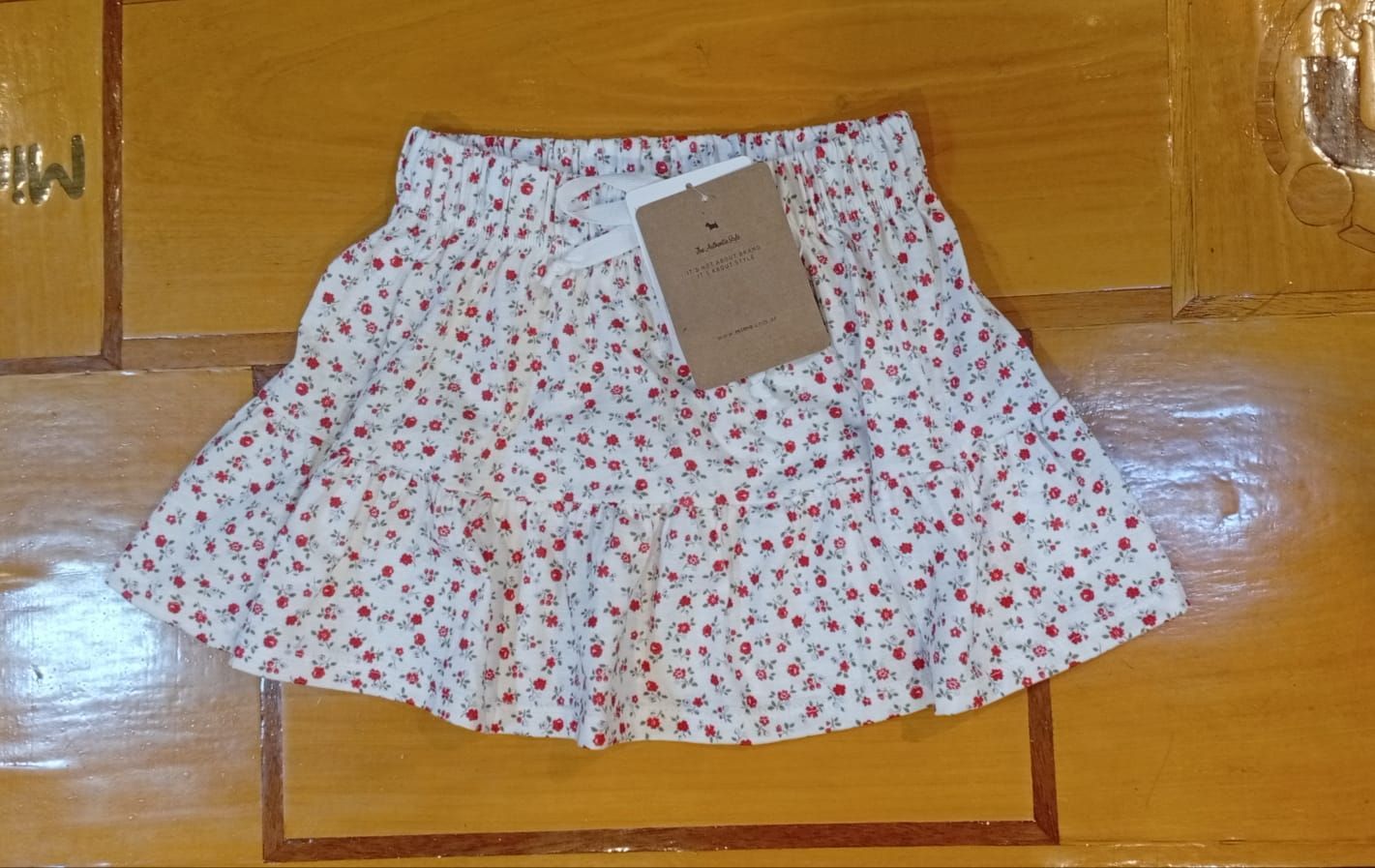 Falda blanca con estampado floral, cintura elástica y etiqueta de precio sobre una superficie de madera.