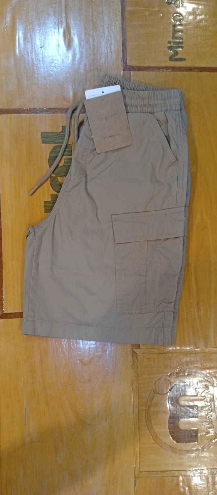 Pantalones cortos cargo color canela con etiqueta, sobre una superficie de madera.